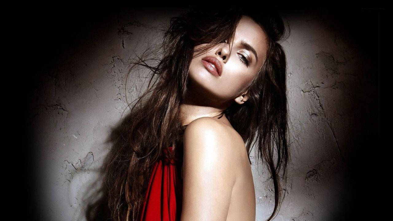 girls 桌布 壁紙 — 一位身穿紅色連衣裙的女性在戲劇性的聚光燈下，靠著紋理牆壁，頭髮隨風飄揚。