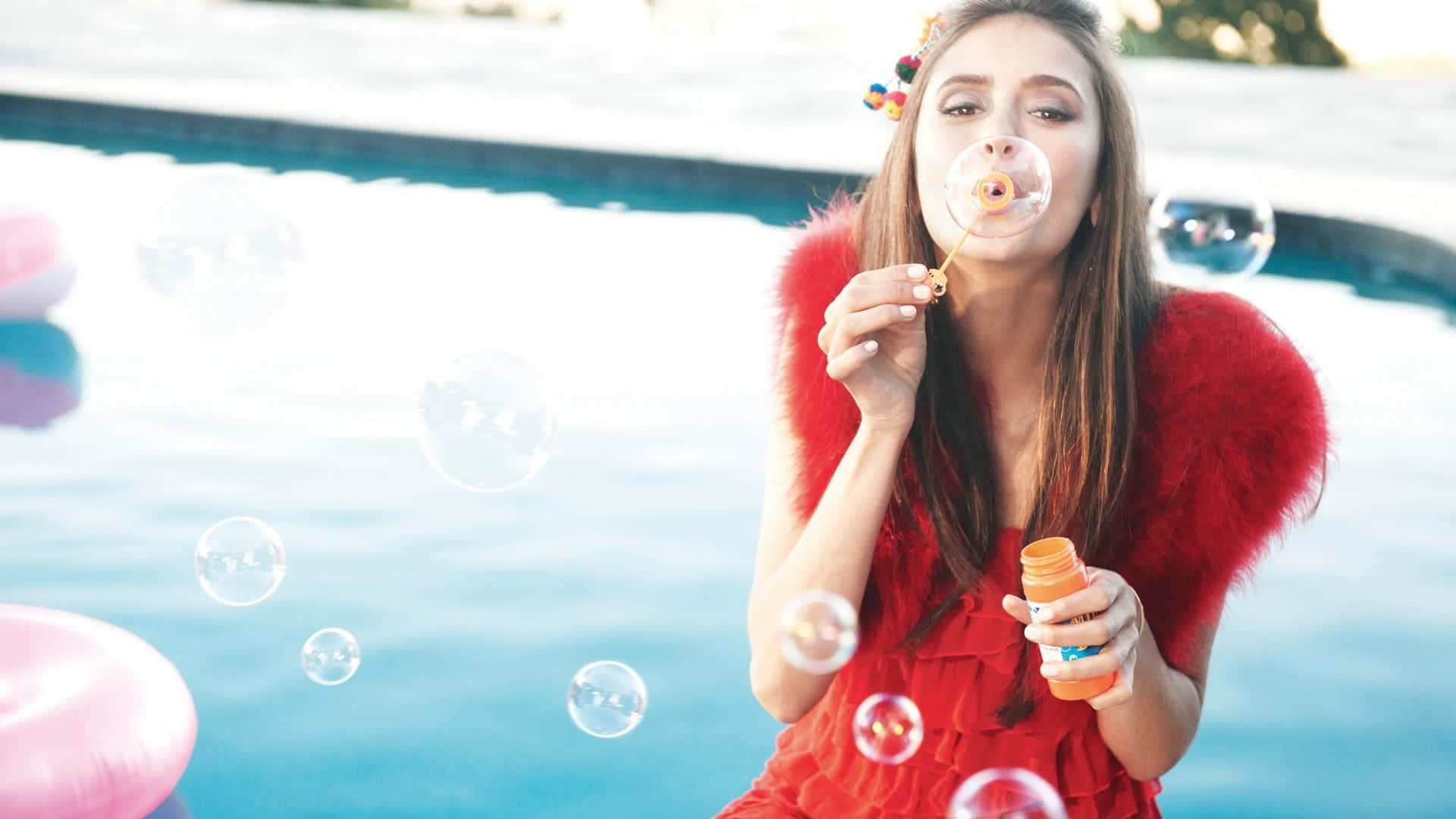 Bubbles 桌布 壁紙 — 一位身穿紅色連衣裙的女性在游泳池旁吹泡泡，附近漂浮著粉紅色浮具。
