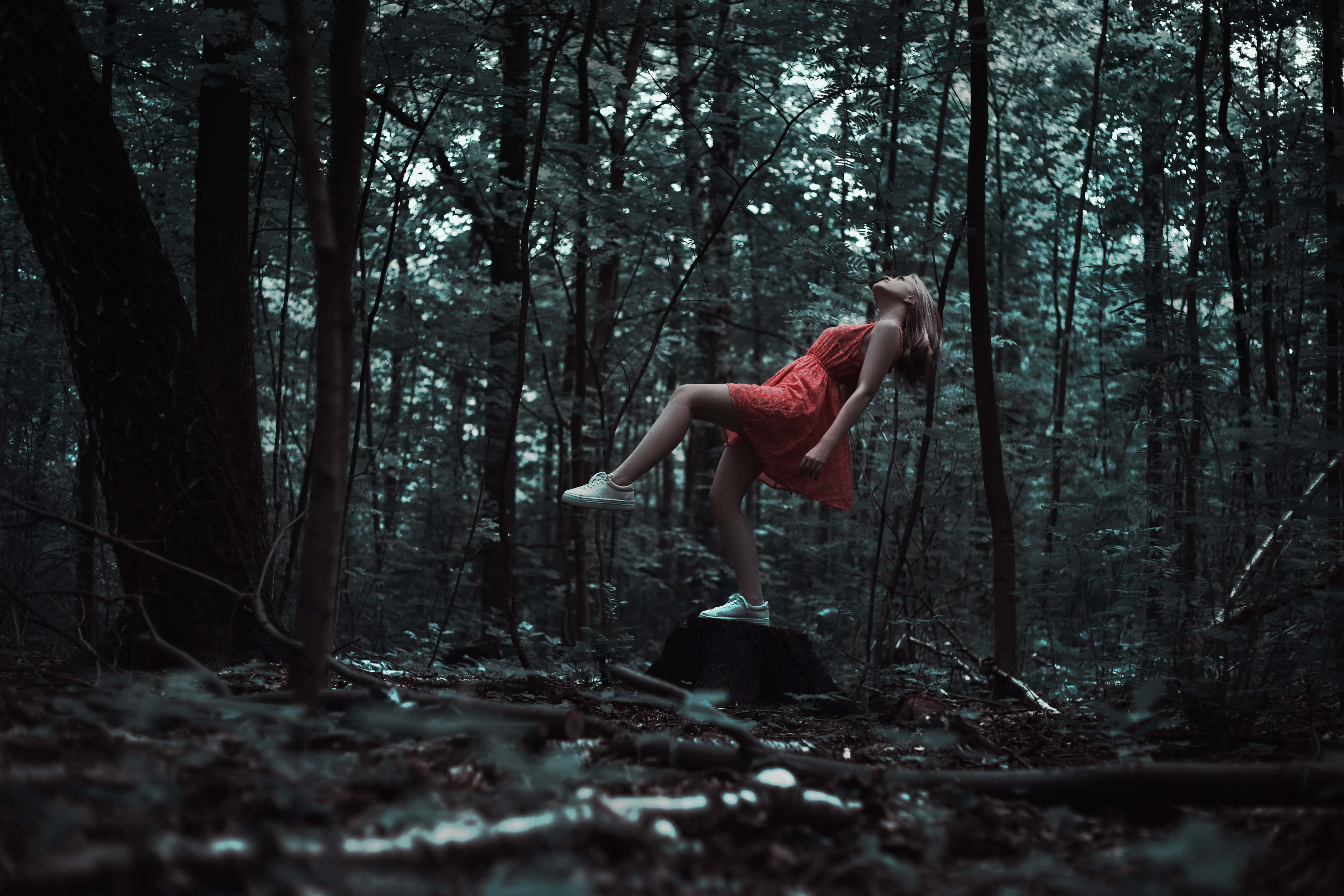 falling 桌布 壁紙 — 一位身穿紅色連衣裙的女性在迷霧籠罩、陰影重重的森林中，優雅地平衡在長滿苔蘚的木頭上。