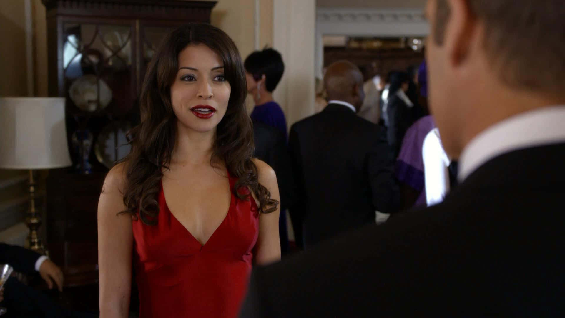 Emmanuelle Vaugier 桌布 壁紙 — 一位身穿紅色連衣裙的女性站在優雅的房間裡，在正式聚會中面對一位身穿西裝的男士。
