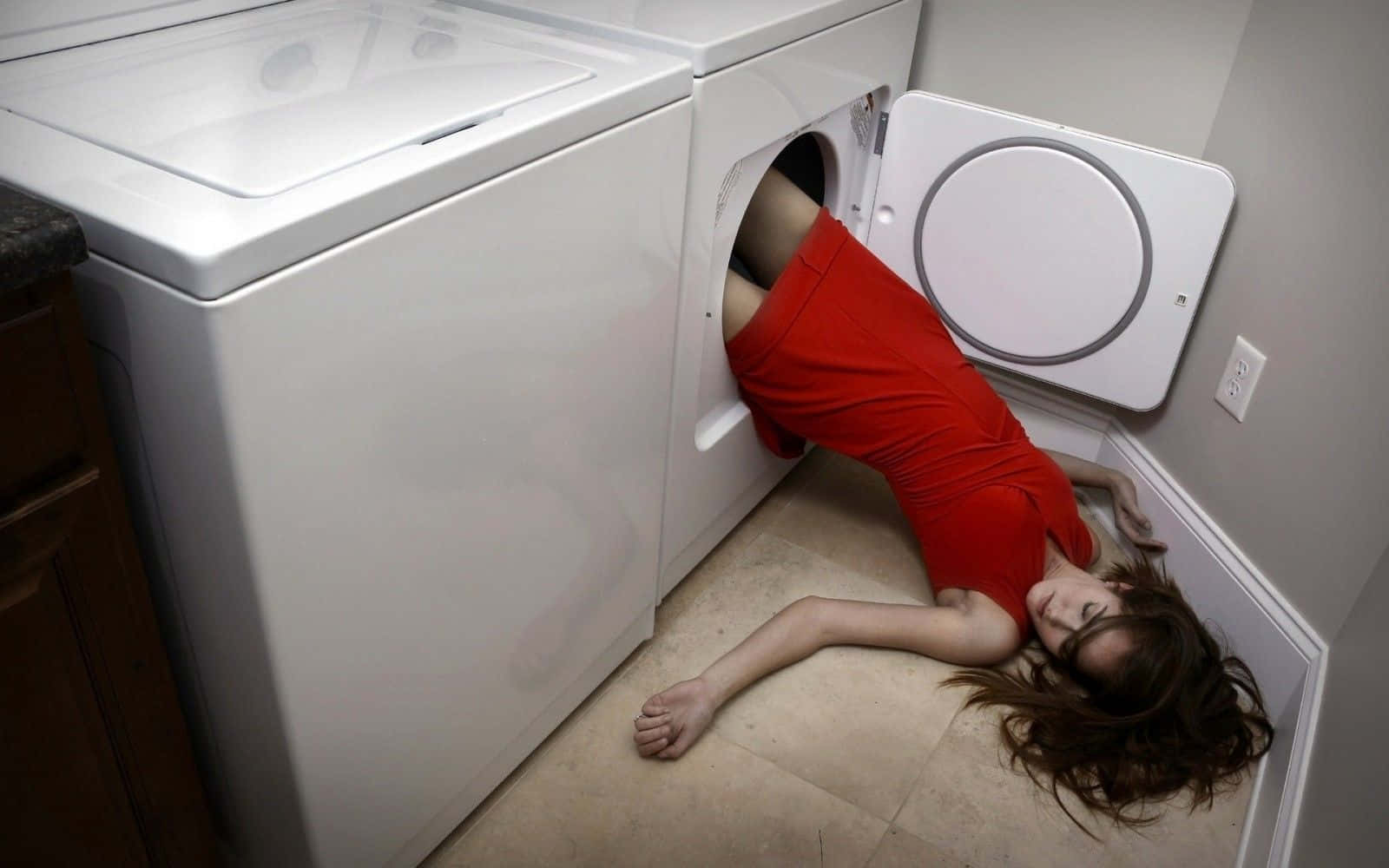 Laundry Room 桌布 壁紙 — 一位身穿紅色連衣裙的女性部分進入洗衣房內白色乾衣機，地板鋪瓷磚，有木櫃。