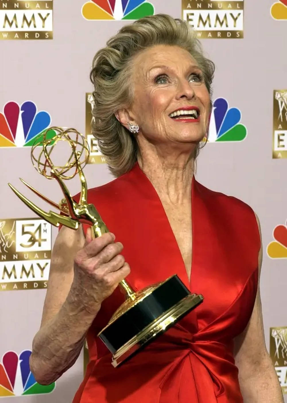 Red Carpet 桌布 壁紙 — 一位身穿紅色連衣裙的年長女性在正式活動中手持金色艾美獎，笑容滿面。