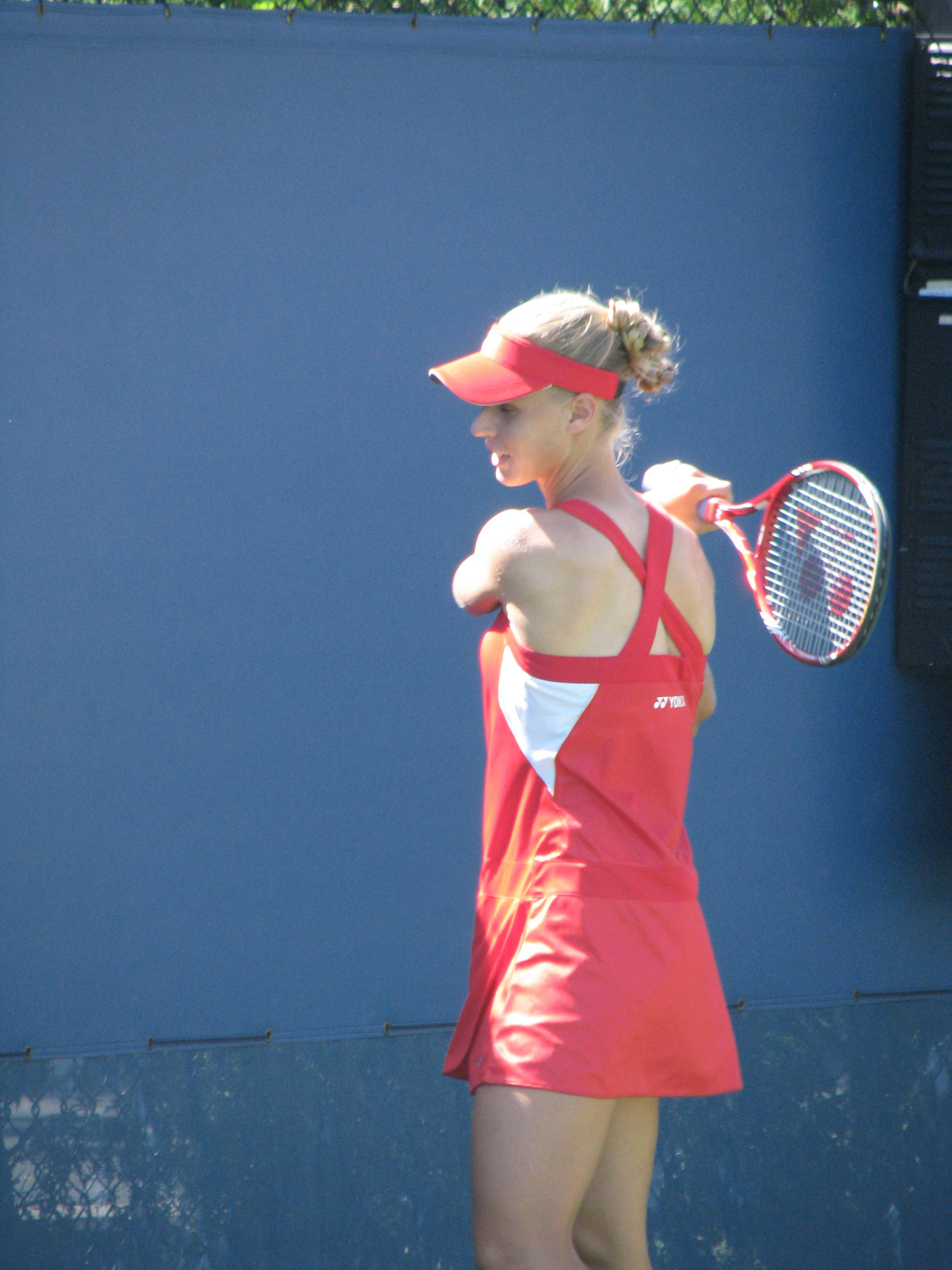 Tennis 桌布 壁紙 — 一位身穿紅色運動服的女性網球選手在明亮的陽光下，準備對著純藍色的牆壁發球。