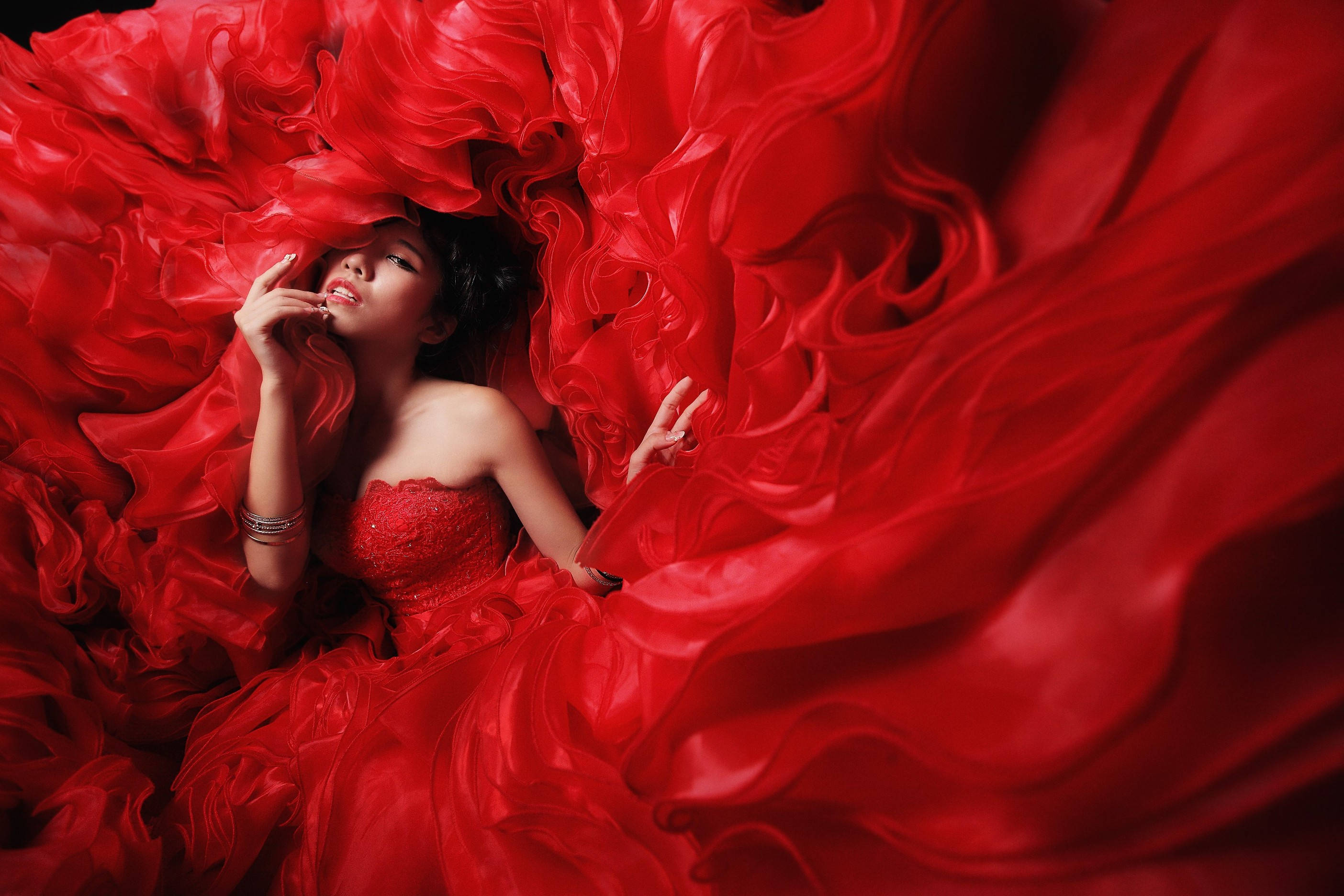 Asian Woman 桌布 壁紙 — 一位身穿紅色長袍的女性，沉浸在一片流動的深紅色布料海洋中，目光向上，帶著寧靜的優雅。