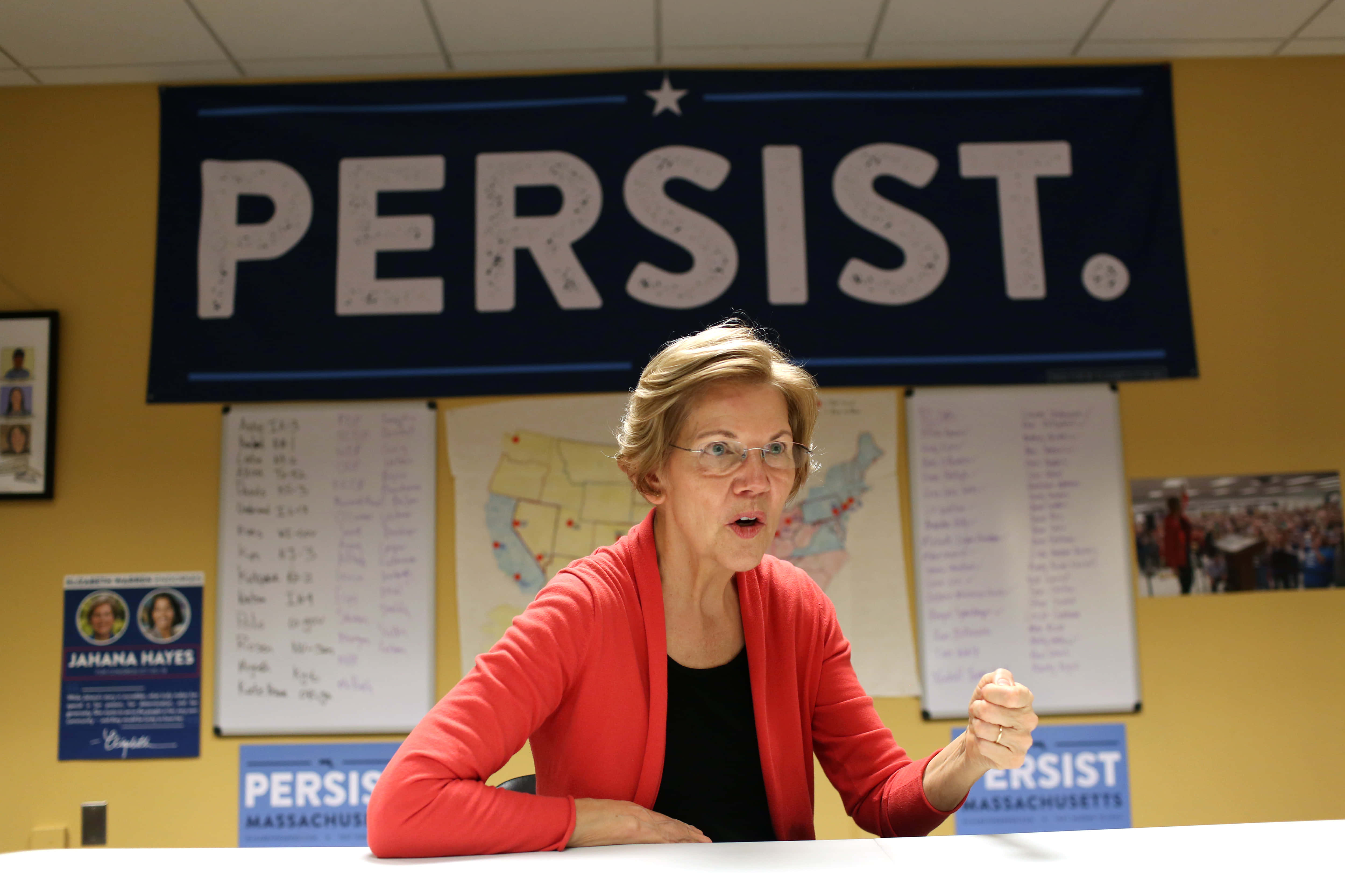 人物 桌布 壁紙 — 一位身穿紅色開襟毛衣的女性在「PERSIST.」橫幅下的競選桌前熱情演講。