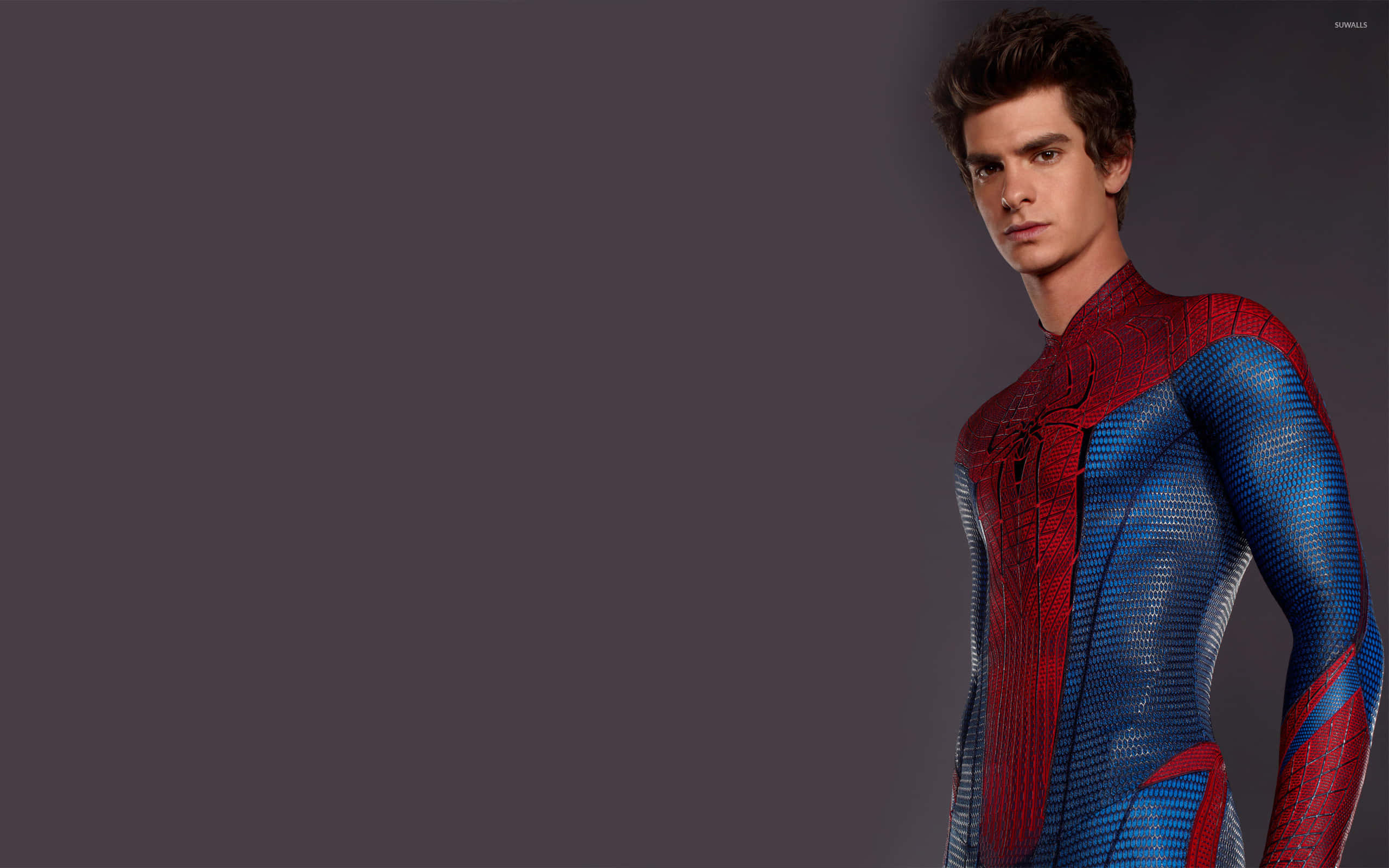 Andrew Garfield Spider Man 桌布 壁紙 — 一位身穿紅藍紋理西裝的超級英雄自信地站在純深灰色背景前。