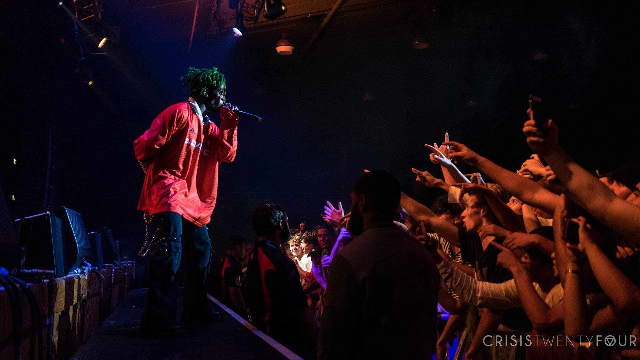 Lil Uzi Desktop 桌布 壁紙 — 一位身穿紅衫的表演者在舞台上對著麥克風唱歌，粉絲們在昏暗的演唱會燈光下手機伸出。