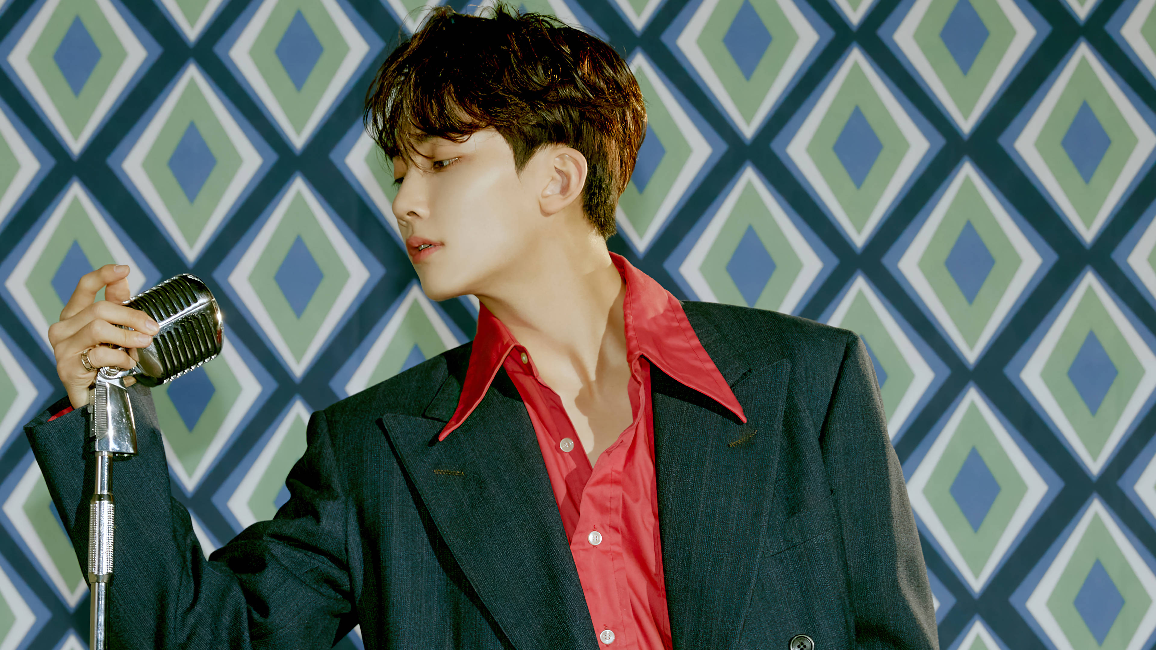 yoon jeonghan 桌布 壁紙 — 一位身穿紅襯衫和深色西裝的年輕男子，手持復古麥克風，背景是鮮明的幾何圖案牆壁。