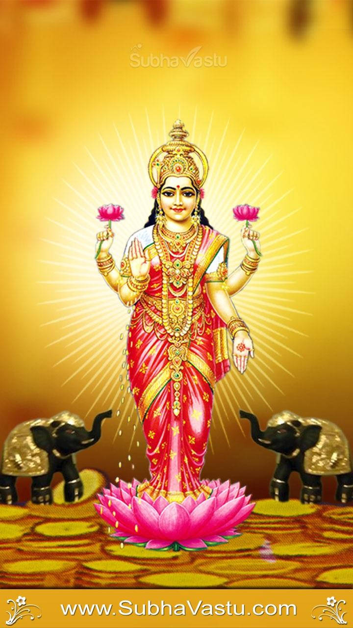 Lakshmi 桌布 壁紙 — 一位身穿紅金服飾、光芒四射的印度教女神站在粉紅蓮花上，兩側有兩頭大象，背景是閃耀的金色光芒。