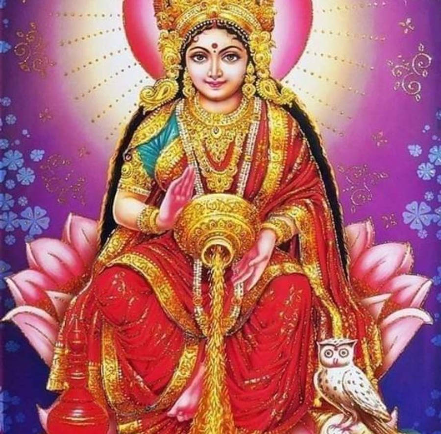 Lakshmi Devi 桌布 壁紙 — 一位身穿紅金服飾的神聖女神優雅地坐在粉紅蓮花上，身旁有一隻貓頭鷹，背景是耀眼的紫色和金色。