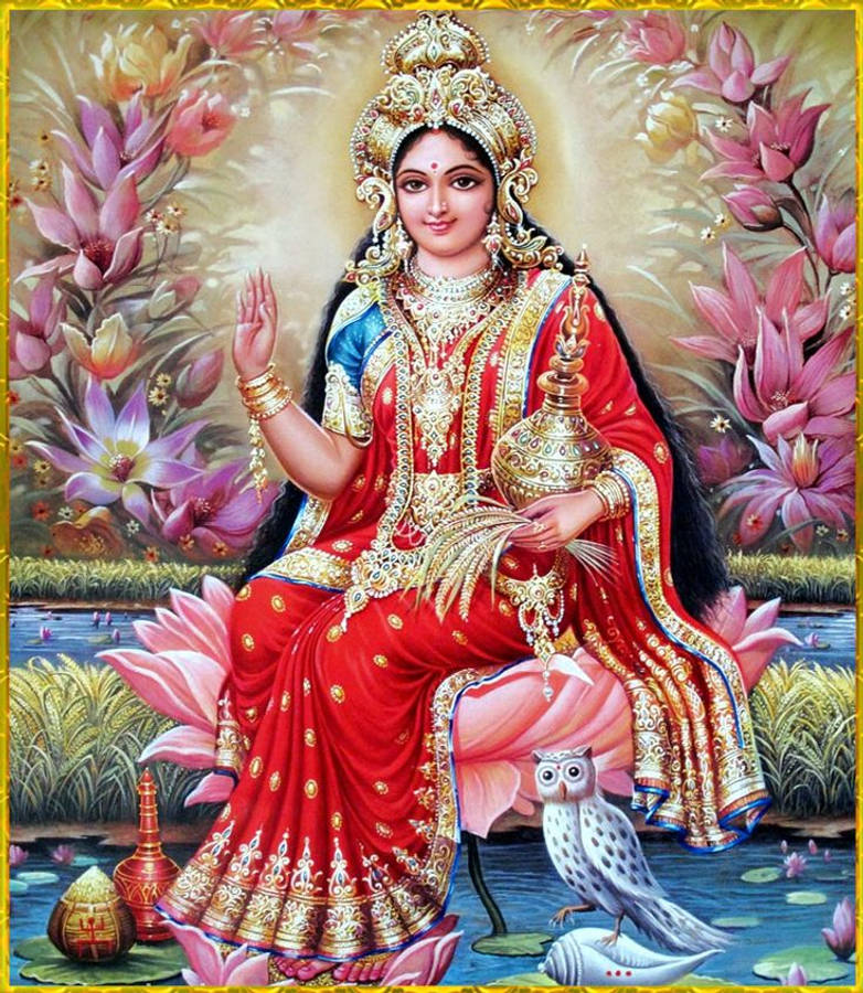 Lakshmi Devi 桌布 壁紙 — 一位身穿紅金服飾的神聖女神優雅地坐在粉紅蓮花上，周圍環繞著盛開的花朵和一隻貓頭鷹。