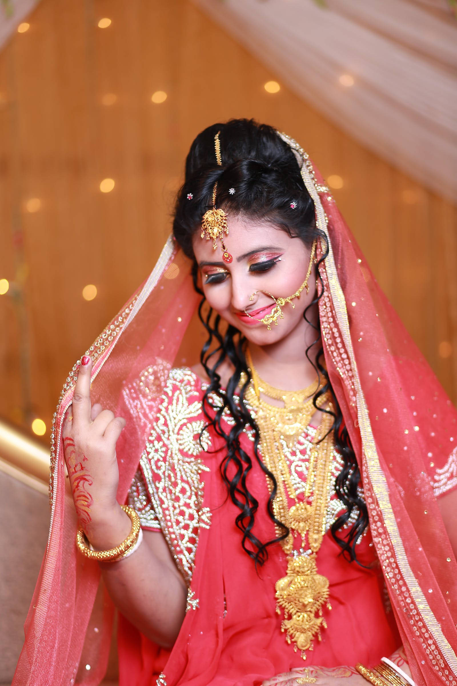 Indian 桌布 壁紙 — 一位身穿紅金色傳統服飾、光彩照人的新娘，佩戴精緻珠寶和指甲花，溫柔微笑。