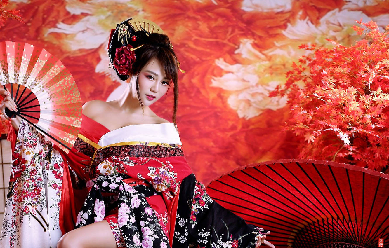 Geisha 桌布 壁紙 — 一位身穿紅黑花卉和服的女士，手持華麗扇子，背景是火紅的秋葉。