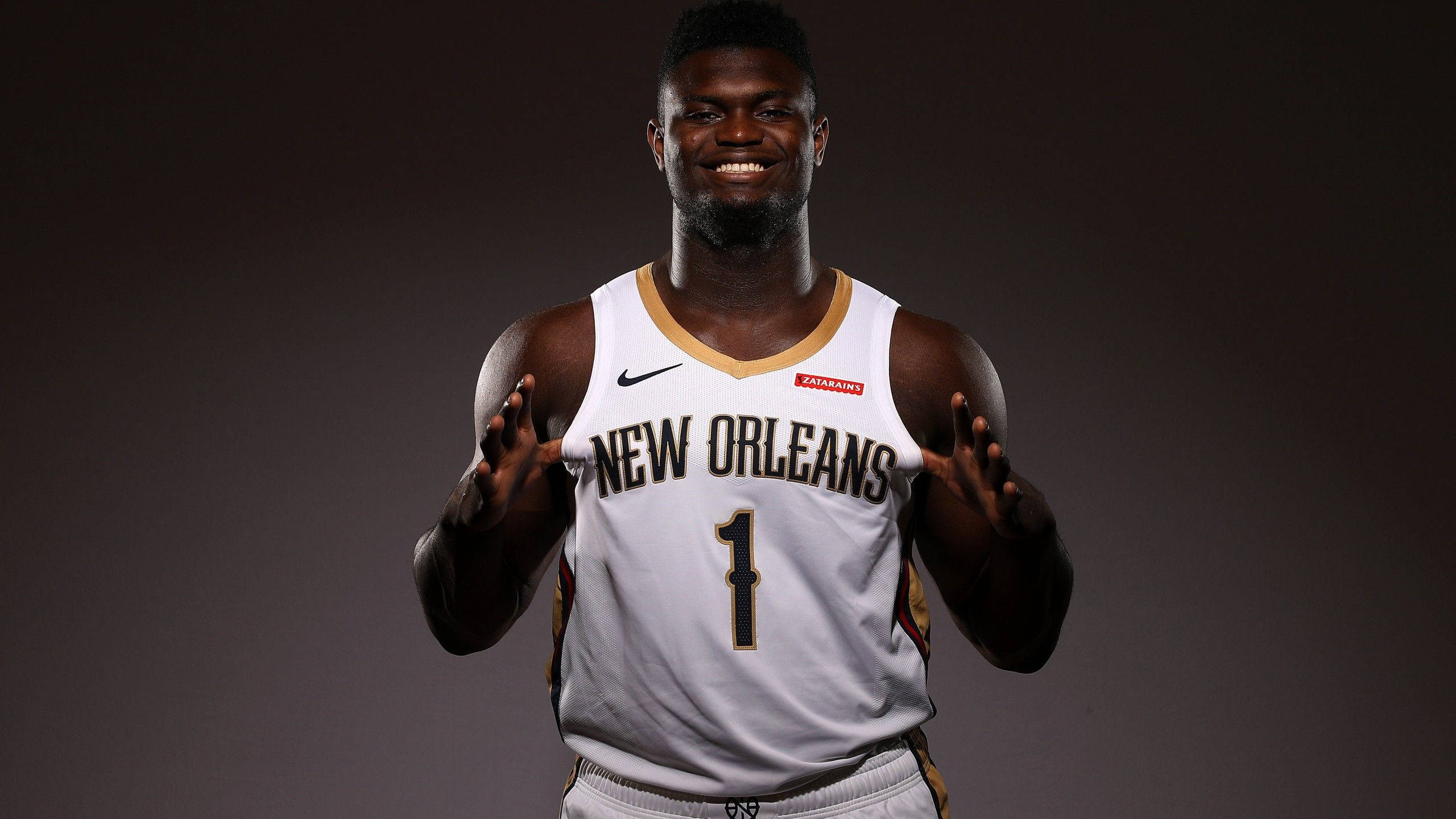 Zion 桌布 壁紙 — 一位身穿紐奧良球衣、號碼一的籃球運動員面帶微笑，在深色攝影棚背景前自信地擺姿勢。