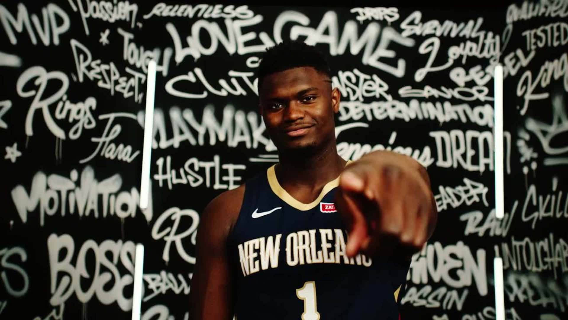 Zion 桌布 壁紙 — 一位身穿紐奧良球衣的自信籃球運動員，在充滿激勵話語的塗鴉牆前向前指。