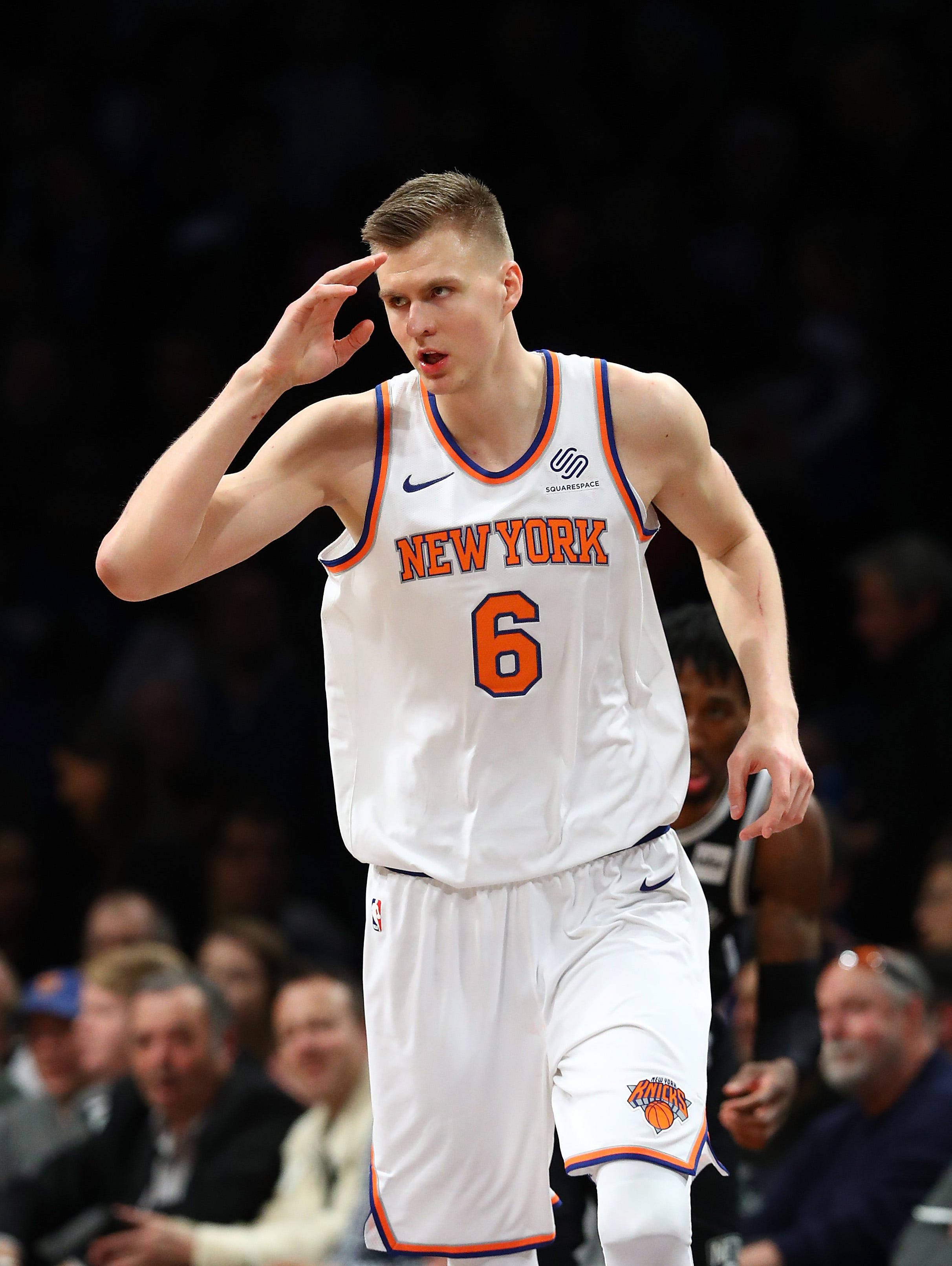 Kristaps Porzingis 桌布 壁紙 — 一位身穿紐約尼克隊6號球衣的籃球運動員在場館燈光下於比賽中向觀眾致敬。