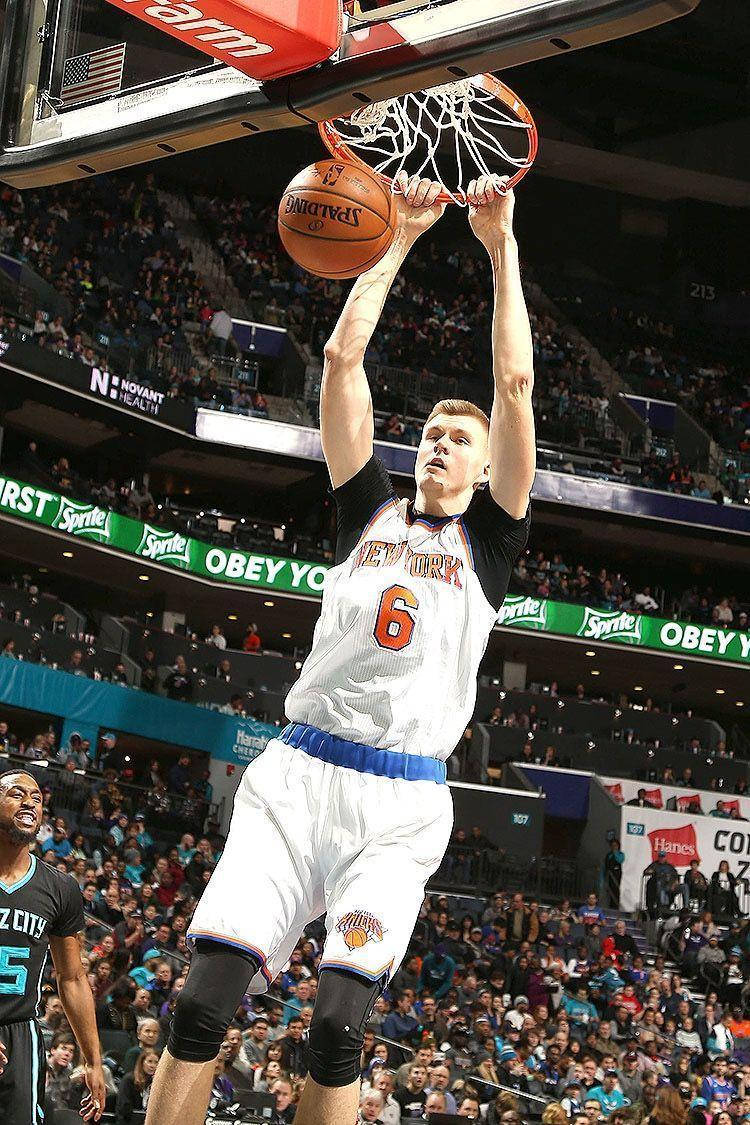 Kristaps Porzingis 桌布 壁紙 — 一位身穿紐約尼克隊球衣的籃球運動員，在座無虛席的場館比賽中，以高度專注力灌籃。