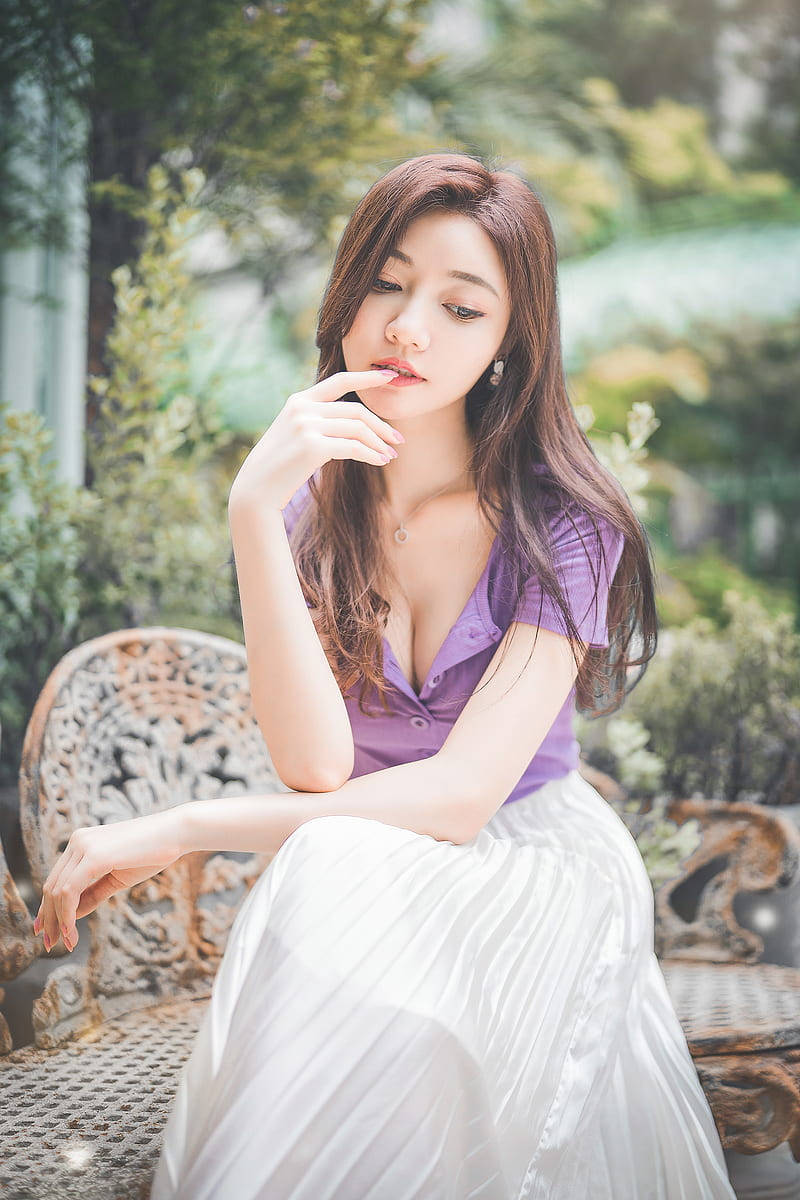 美女 桌布 壁紙 — 一位身穿紫色上衣和白色裙子的女士，坐在華麗的花園長椅上，周圍綠意盎然，若有所思。