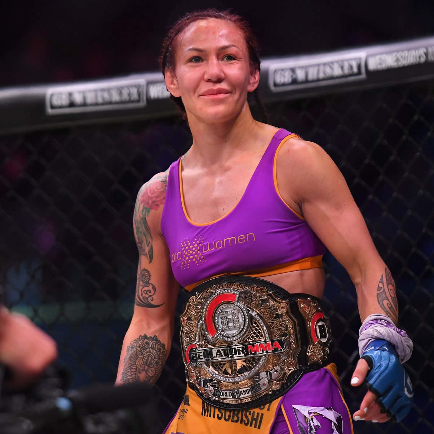 martial arts 桌布 壁紙 — 一位身穿紫色上衣的勝利女性MMA拳手在八角籠內微笑著手持冠軍腰帶。
