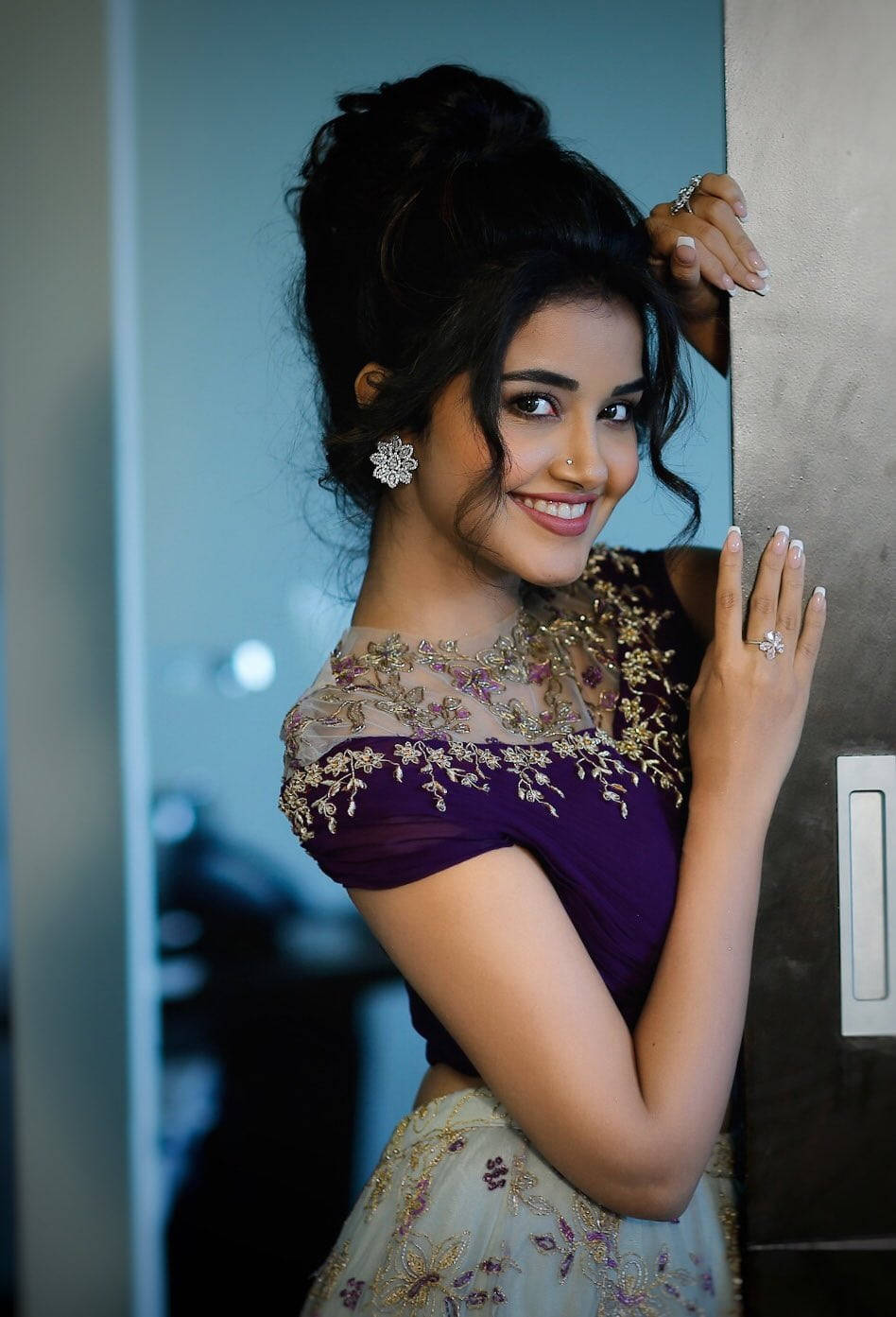 anupama parameswaran 桌布 壁紙 — 一位身穿紫色和奶油色刺繡服裝的容光煥發的女性，在室內靠牆微笑。