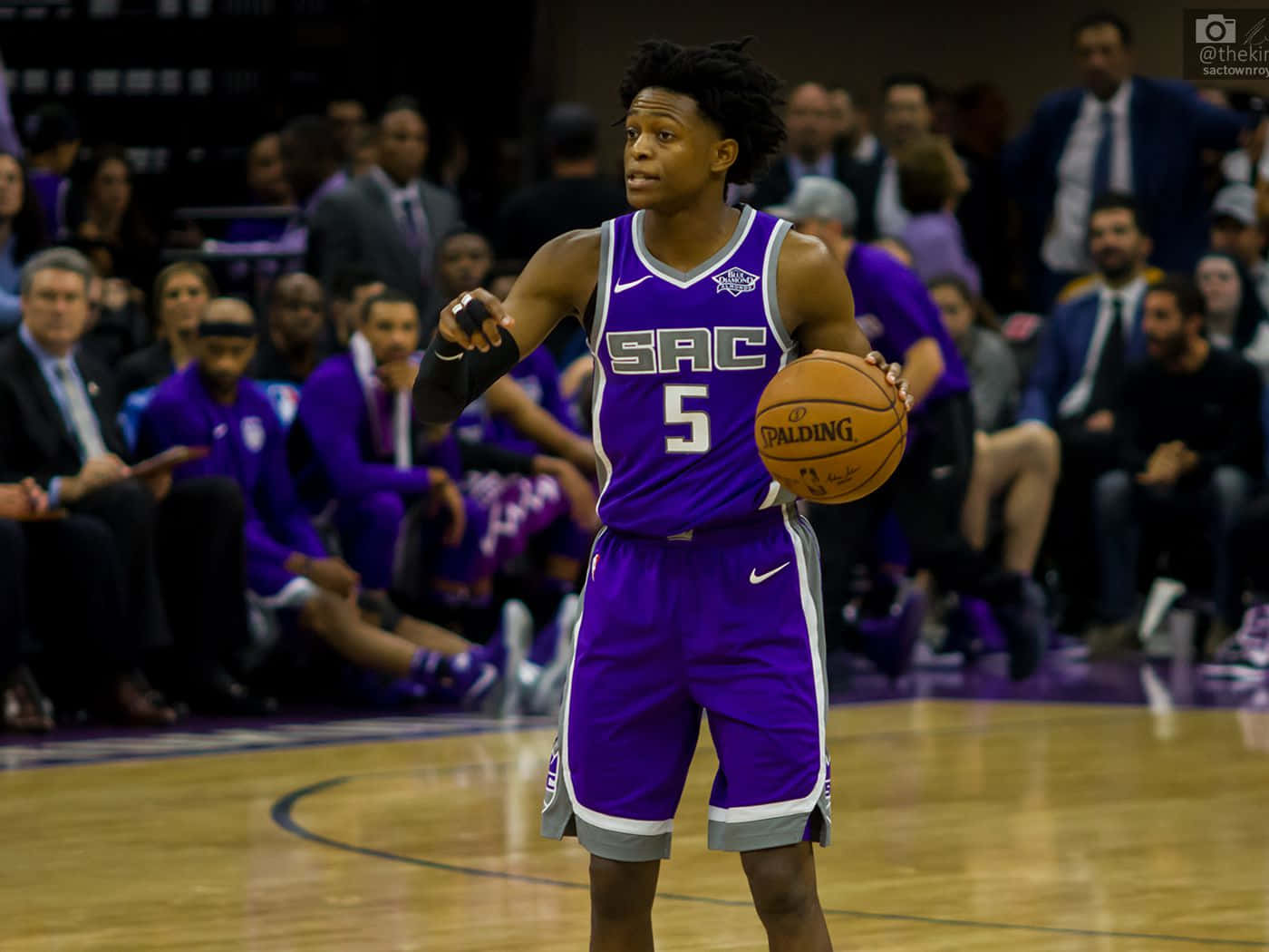 NBA 桌布 壁紙 — 一位身穿紫色沙加緬度國王隊球衣的籃球運動員在硬木球場上運著Spalding籃球，背景有球迷。