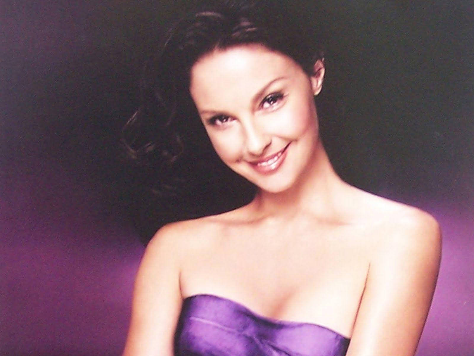 Ashley Judd 桌布 壁紙 — 一位身穿紫色無肩帶連衣裙的女性在紫色漸變背景前溫暖地微笑。