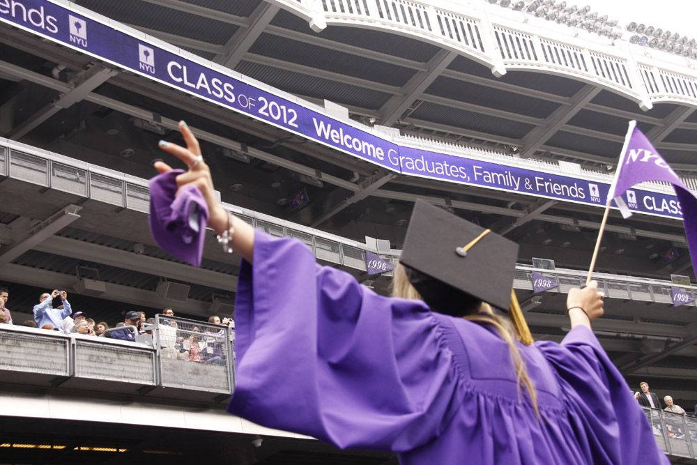 Graduation 桌布 壁紙 — 一位身穿紫色畢業袍和帽的畢業生在體育館畢業典禮上，在「Class of 2012」橫幅下向歡呼的人群揮手。