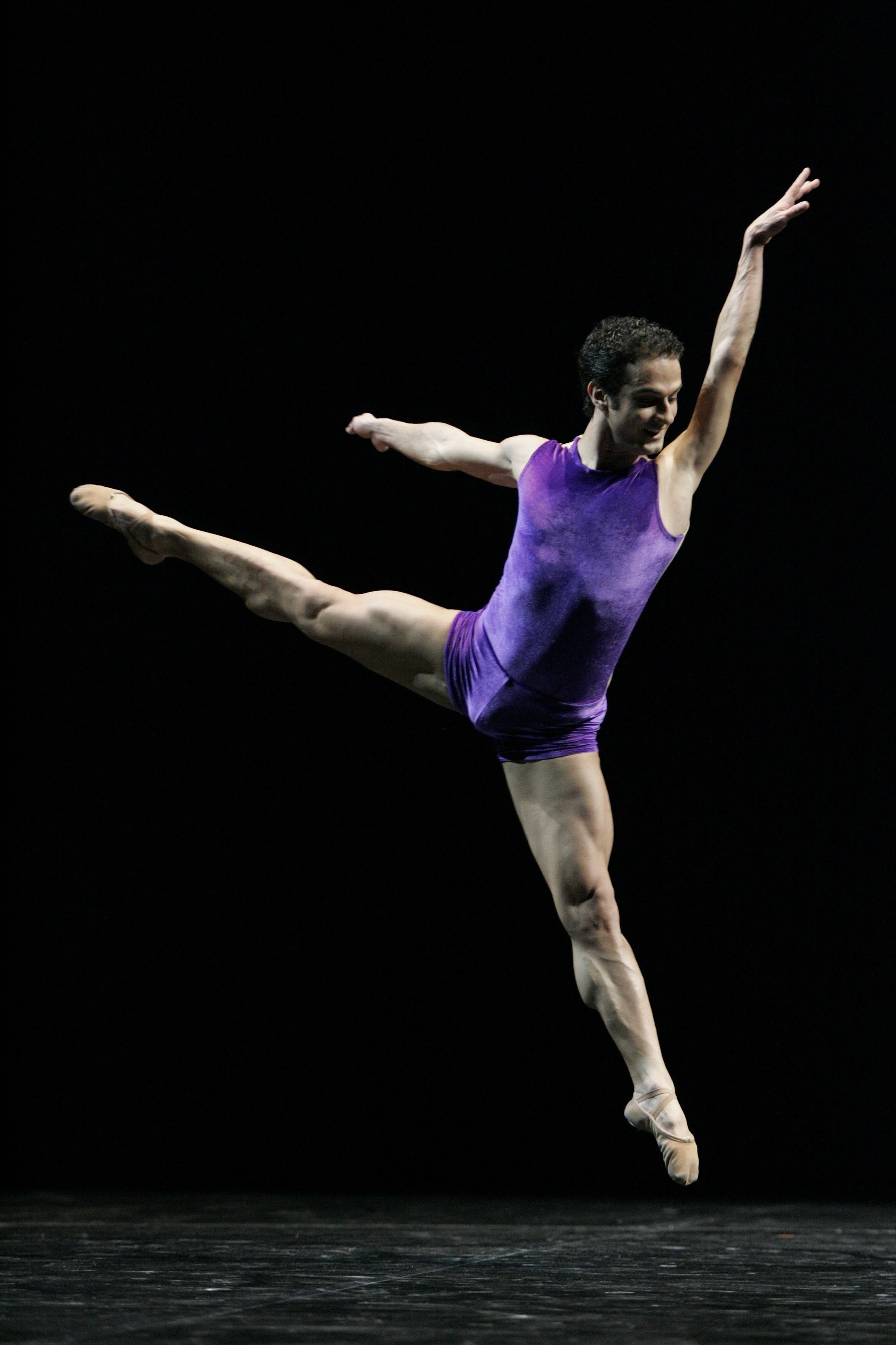 dancer 桌布 壁紙 — 一位身穿紫色緊身衣的男芭蕾舞者在純黑背景下優雅躍起，雙臂伸展，一腿高踢。