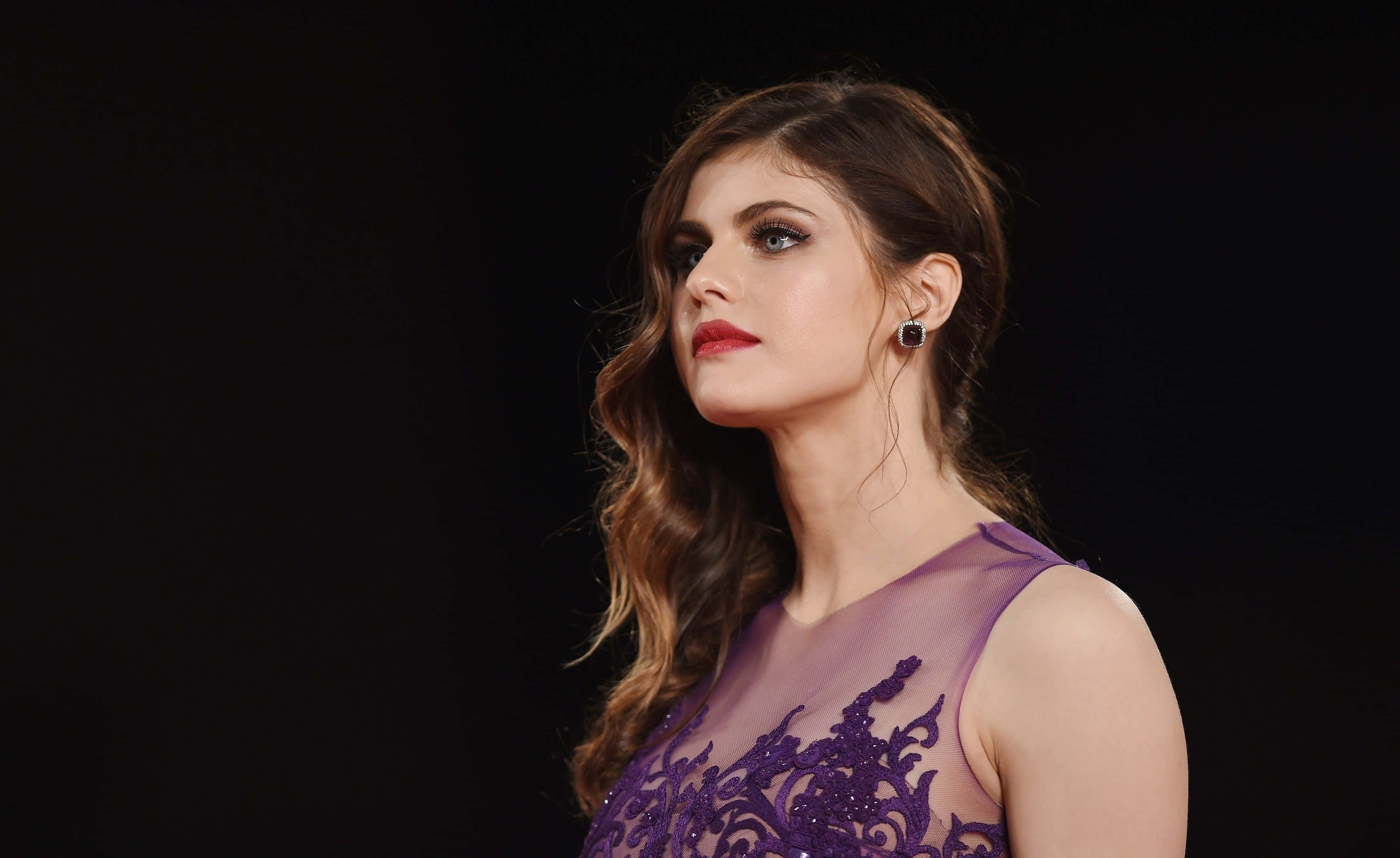 Alexandra Daddario 桌布 壁紙 — 一位身穿紫色蕾絲連衣裙的女性在強烈黑色背景和戲劇性燈光下向上凝視。
