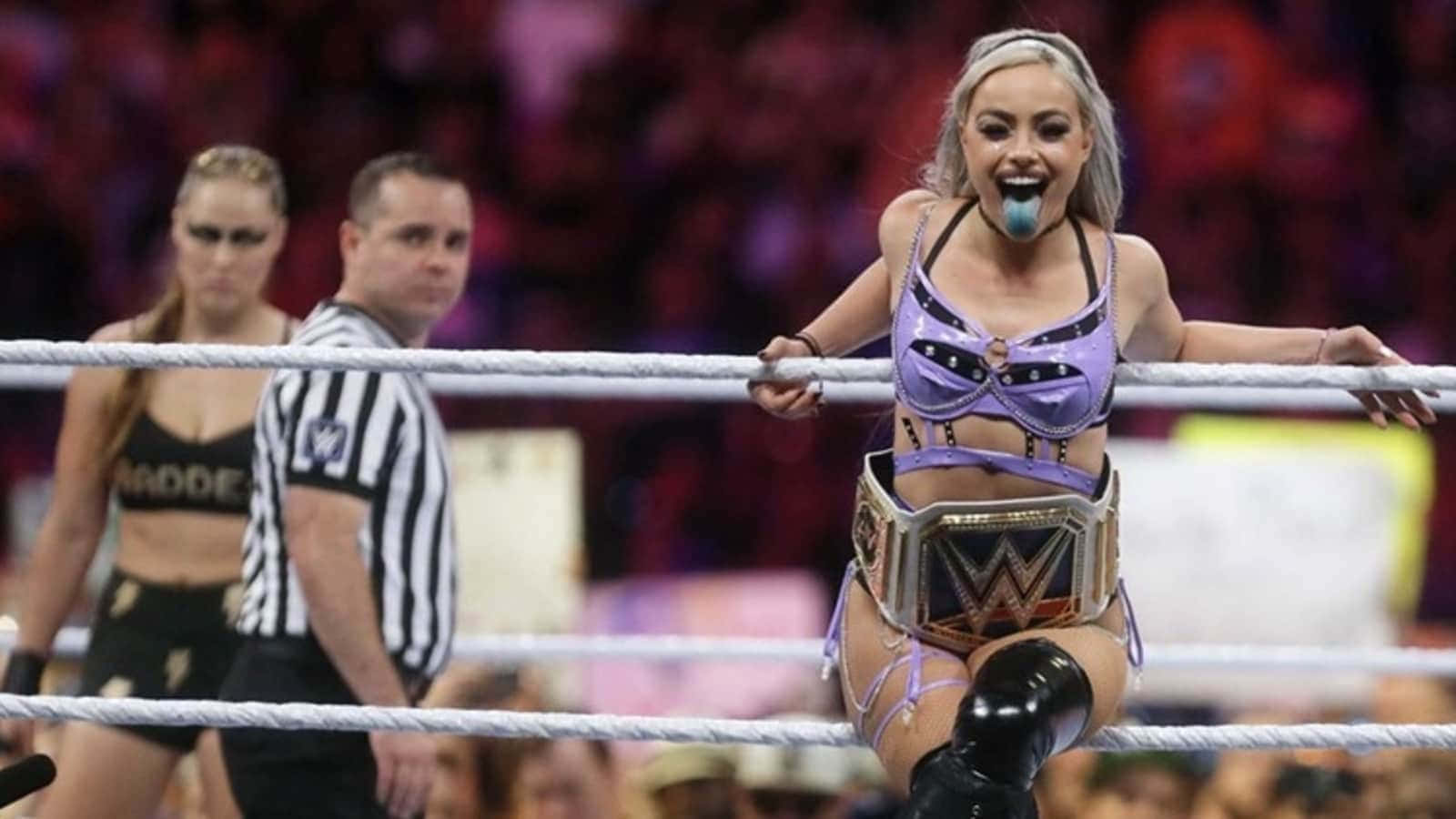 WWE 桌布 壁紙 — 一位身穿紫色裝備的WWE摔角手坐在擂台繩索頂端，手持冠軍腰帶並伸出舌頭。