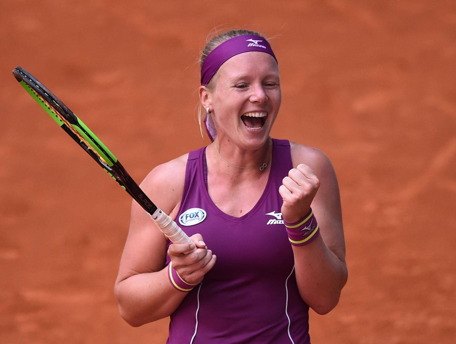 Tennis 桌布 壁紙 — 一位身穿紫色裝備的快樂女網球運動員在紅土場上握緊拳頭、高舉球拍慶祝勝利。