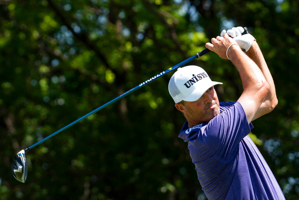 Ryan Palmer 桌布 壁紙 — 一位身穿紫色襯衫和白色帽子的男性高爾夫球手，正專注地揮動藍色球桿，背景是茂密的綠色樹木。