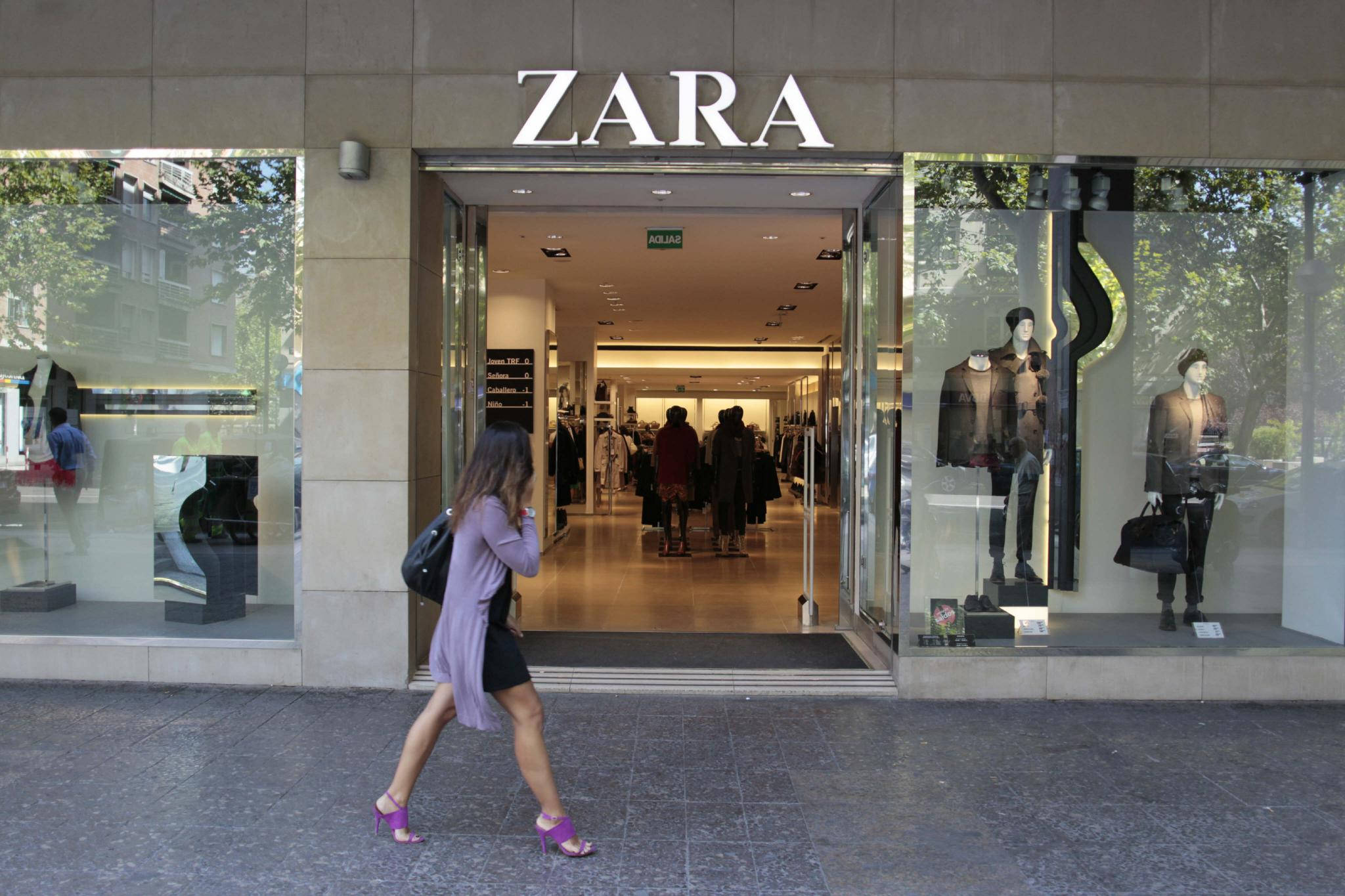 Zara 桌布 壁紙 — 一位身穿紫色連衣裙和粉色高跟鞋的女性走過Zara商店，玻璃櫥窗內展示著人體模型和購物者。