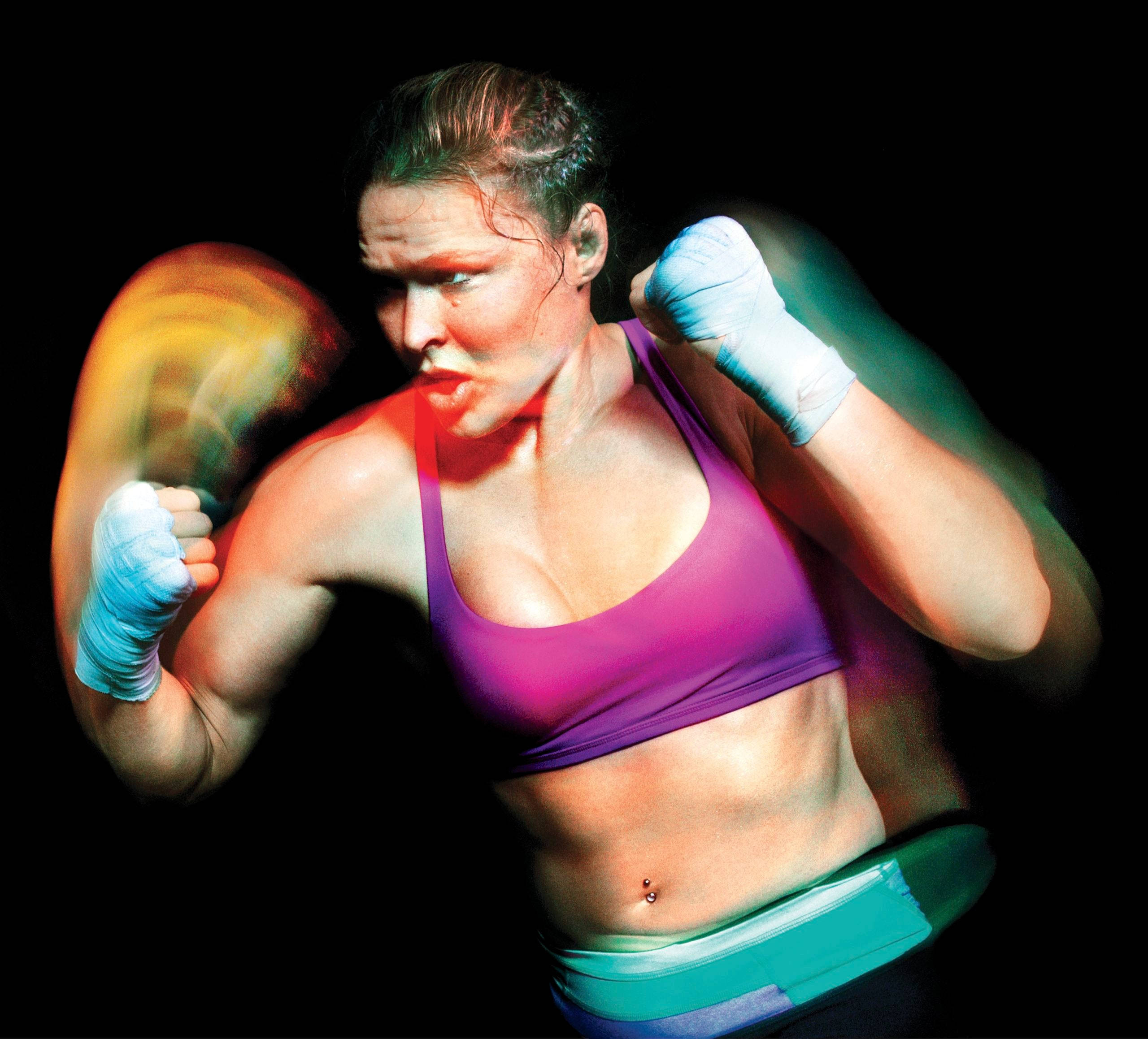 Rousey 桌布 壁紙 — 一位身穿紫色運動胸罩的女拳擊手在黑色背景和彩色燈光下，以動態模糊效果揮出一拳。
