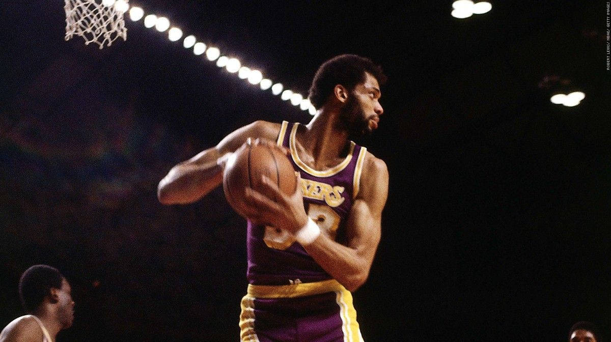 Kareem 桌布 壁紙 — 一位身穿紫金色湖人球衣的籃球運動員在場館燈光下準備投籃，籃框在上方。