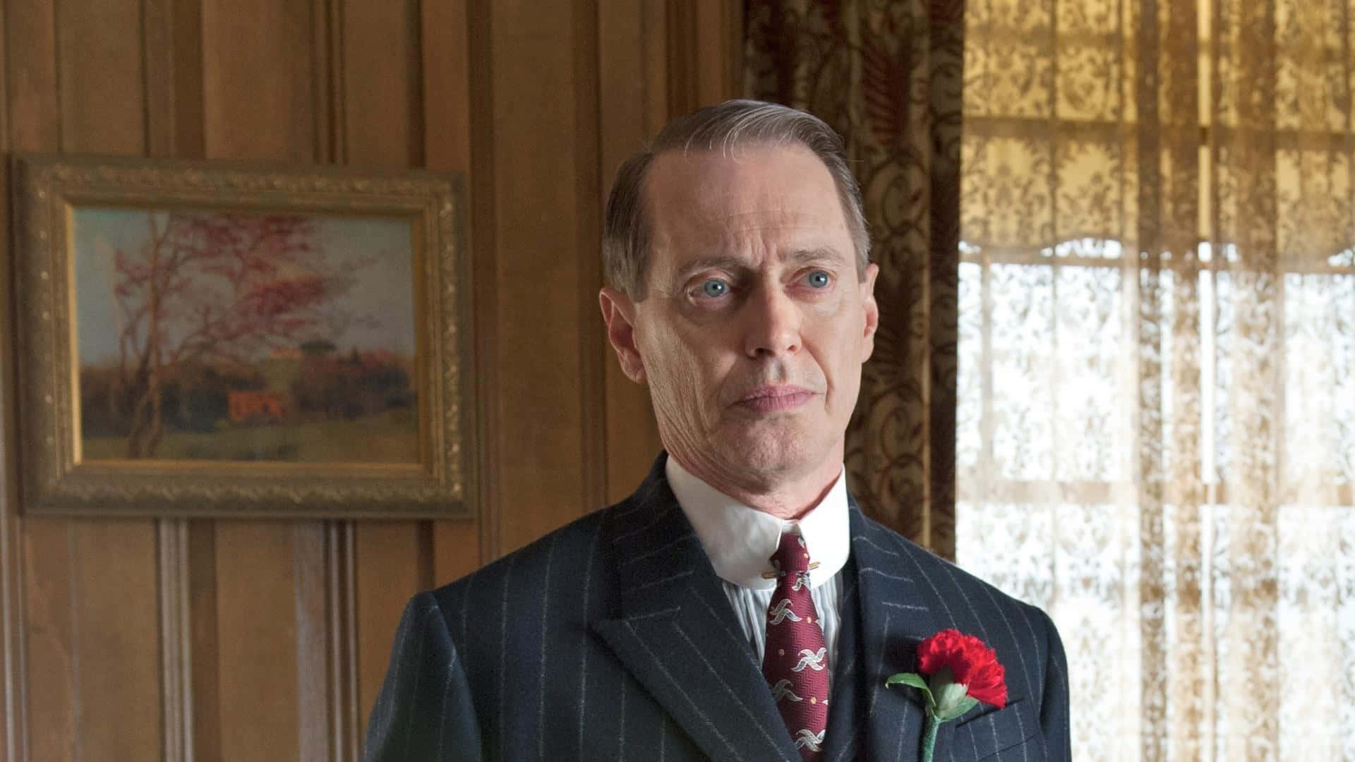 steve buscemi 桌布 壁紙 — 一位身穿細條紋西裝、佩戴紅色康乃馨的男子，站在一個有木鑲板、蕾絲窗簾和裱框畫作的房間裡。