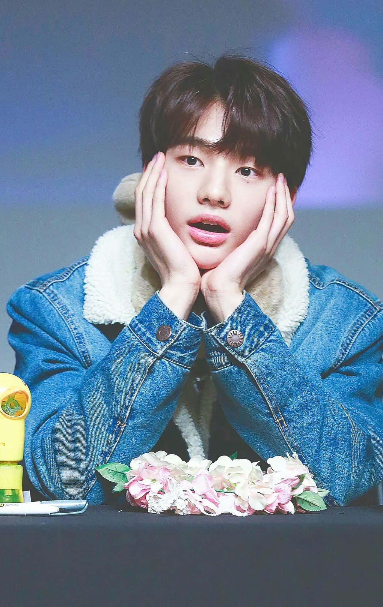 hyunjin 桌布 壁紙 — 一位身穿絨毛領牛仔外套的年輕男子，在一張放有粉紅色花朵的桌子上，用手托著下巴。