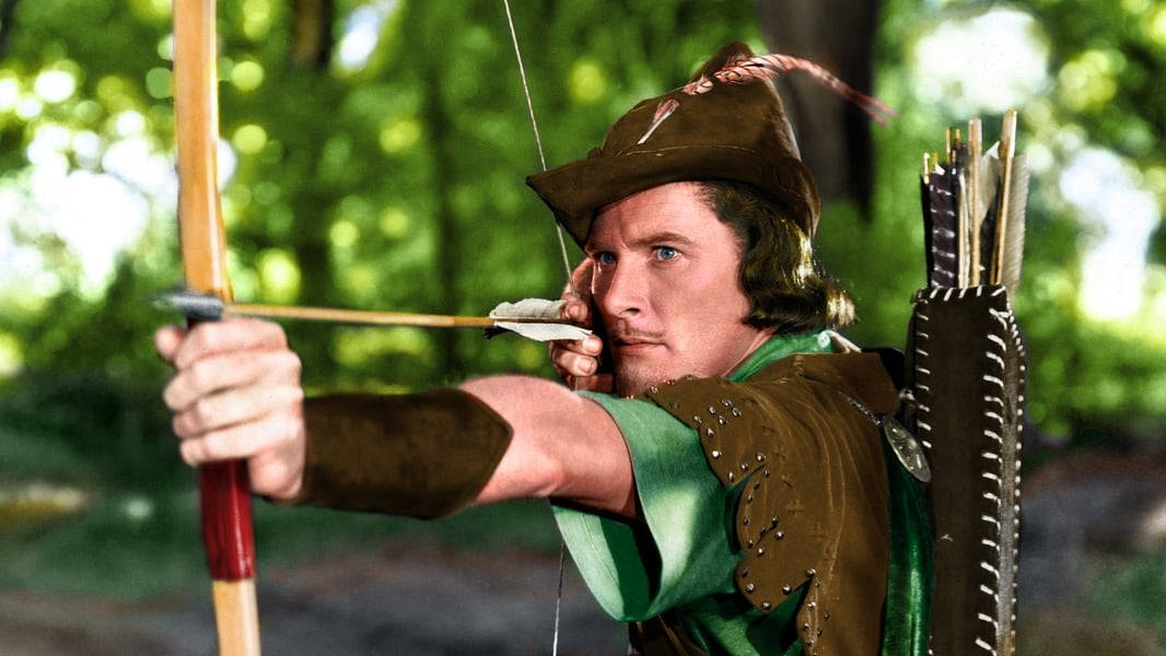 Robin Hood 桌布 壁紙 — 一位身穿綠色和棕色中世紀服裝的專注弓箭手，在陽光普照的森林中拉弓，身後是模糊的綠色樹葉。