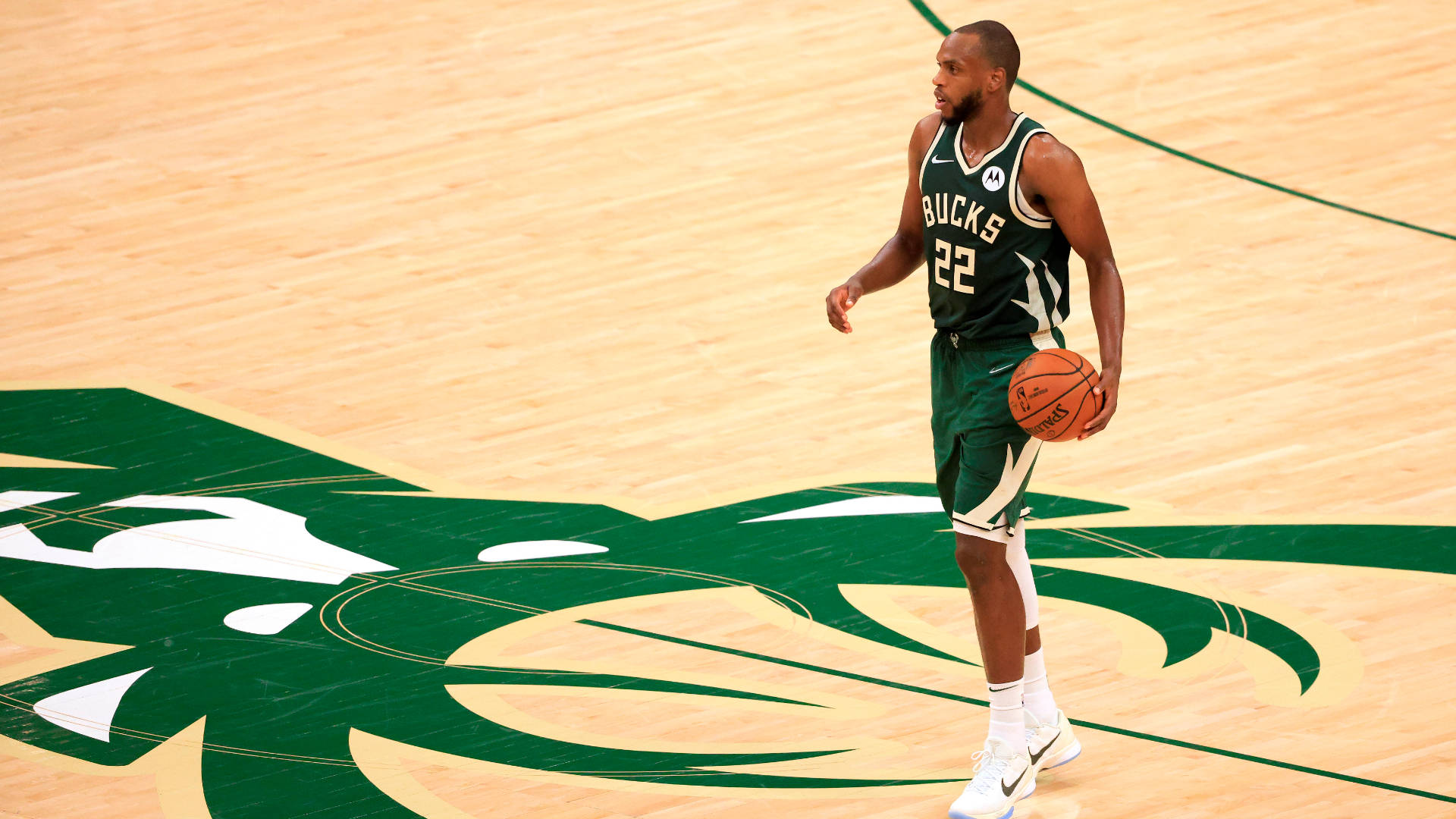 Khris Middleton 桌布 壁紙 — 一位身穿綠色球衣的密爾瓦基公鹿籃球運動員在硬木球場上拿著球，球場上有球隊標誌。