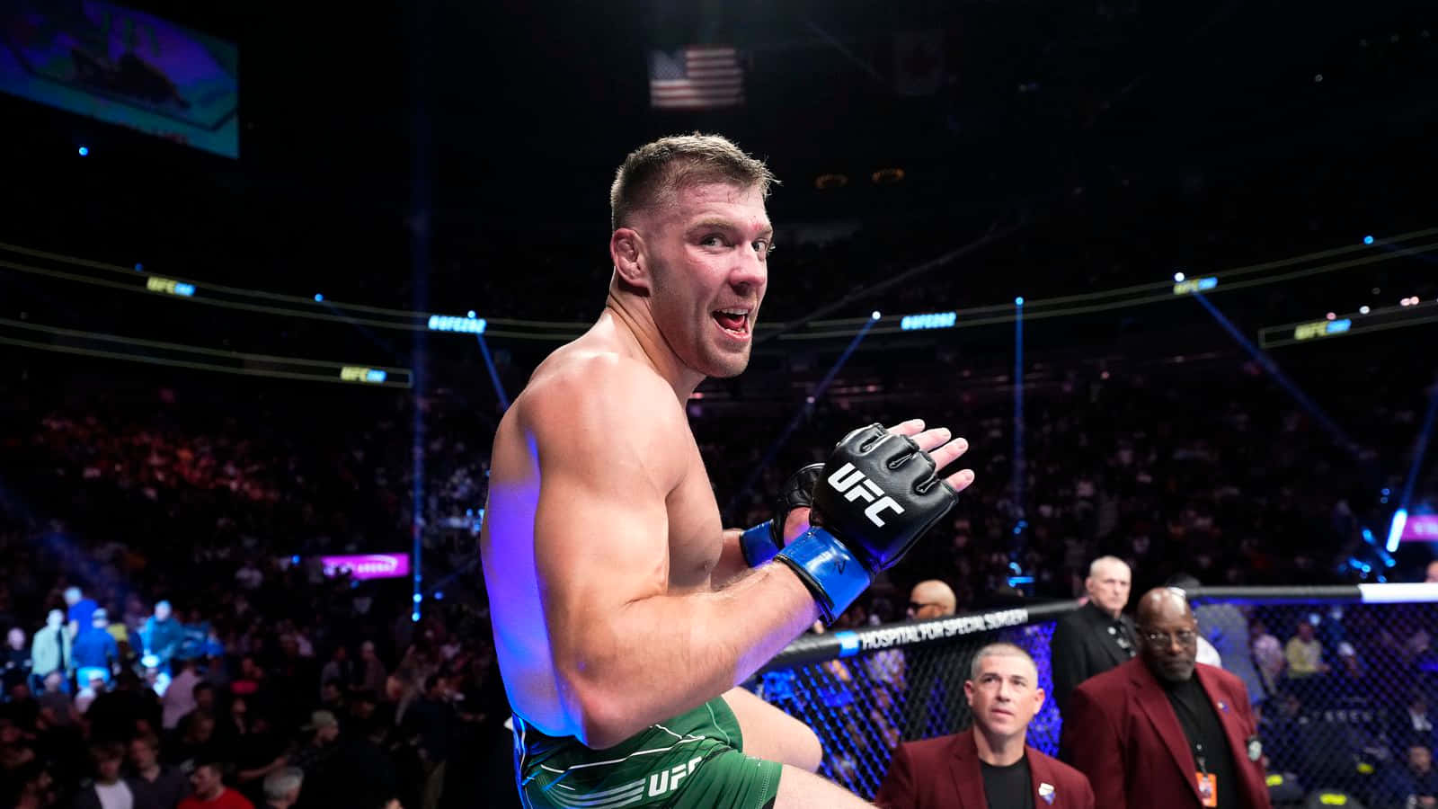 桌布 壁紙 — 一位身穿綠色短褲的UFC勝利者在明亮的場館燈光下於八角籠內慶祝。
