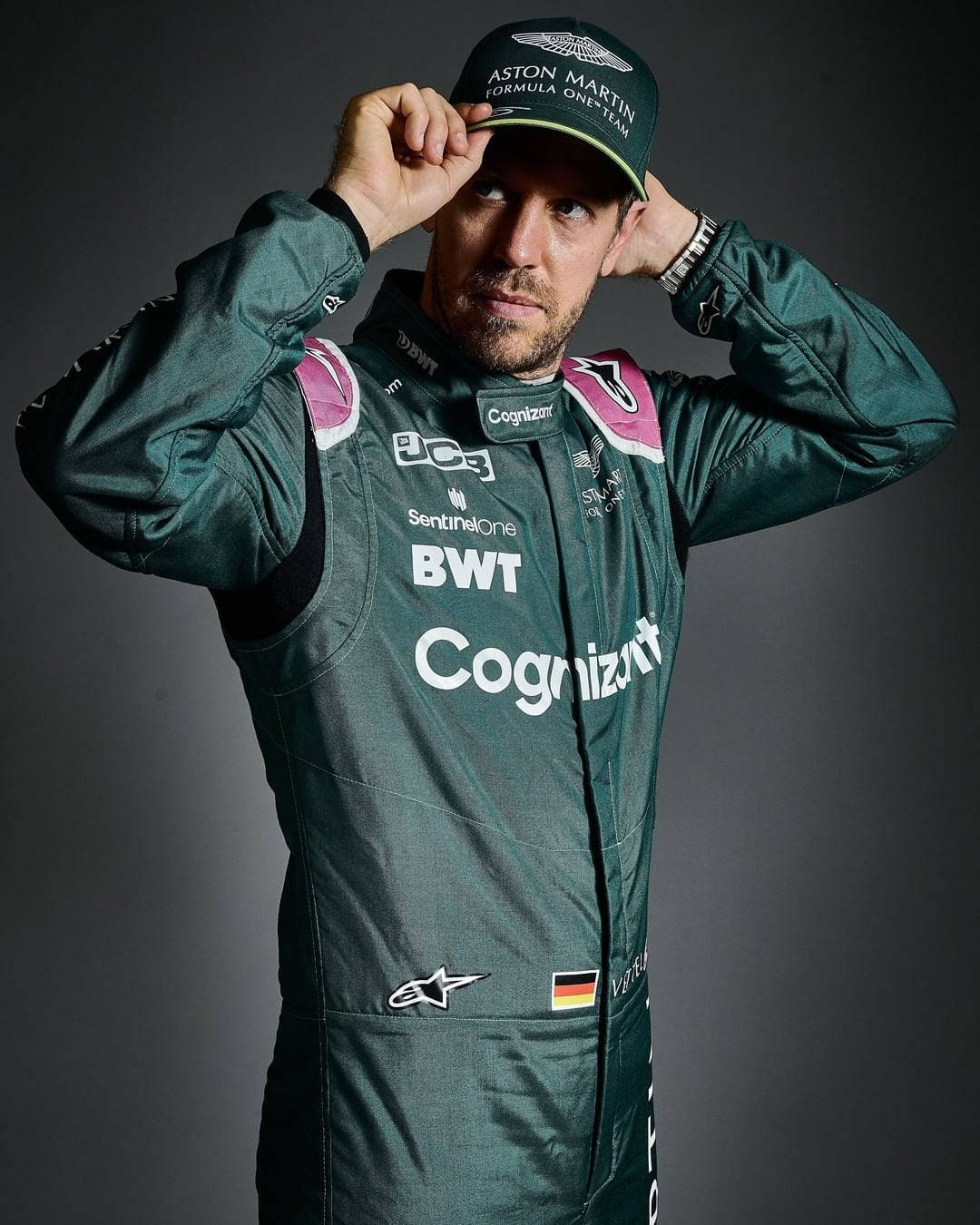sebastian vettel 桌布 壁紙 — 一位身穿綠色賽車服的F1車手在深色攝影棚背景下調整帽子。