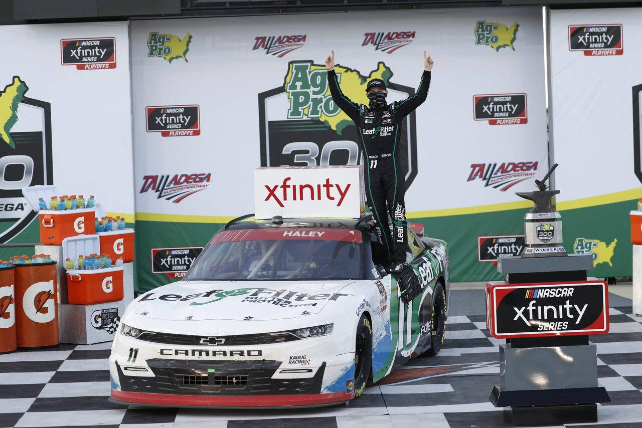 Victory 桌布 壁紙 — 一位身穿綠色賽車服的NASCAR車手在Talladega的方格頒獎台上站在他的白色雪佛蘭Camaro上慶祝。