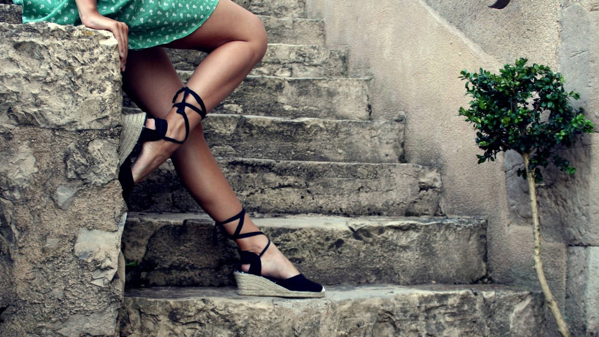 stairs 桌布 壁紙 — 一位身穿綠色連衣裙和黑色繫帶楔形涼鞋的女性，在風化的石階上休憩，旁邊有一棵小樹。