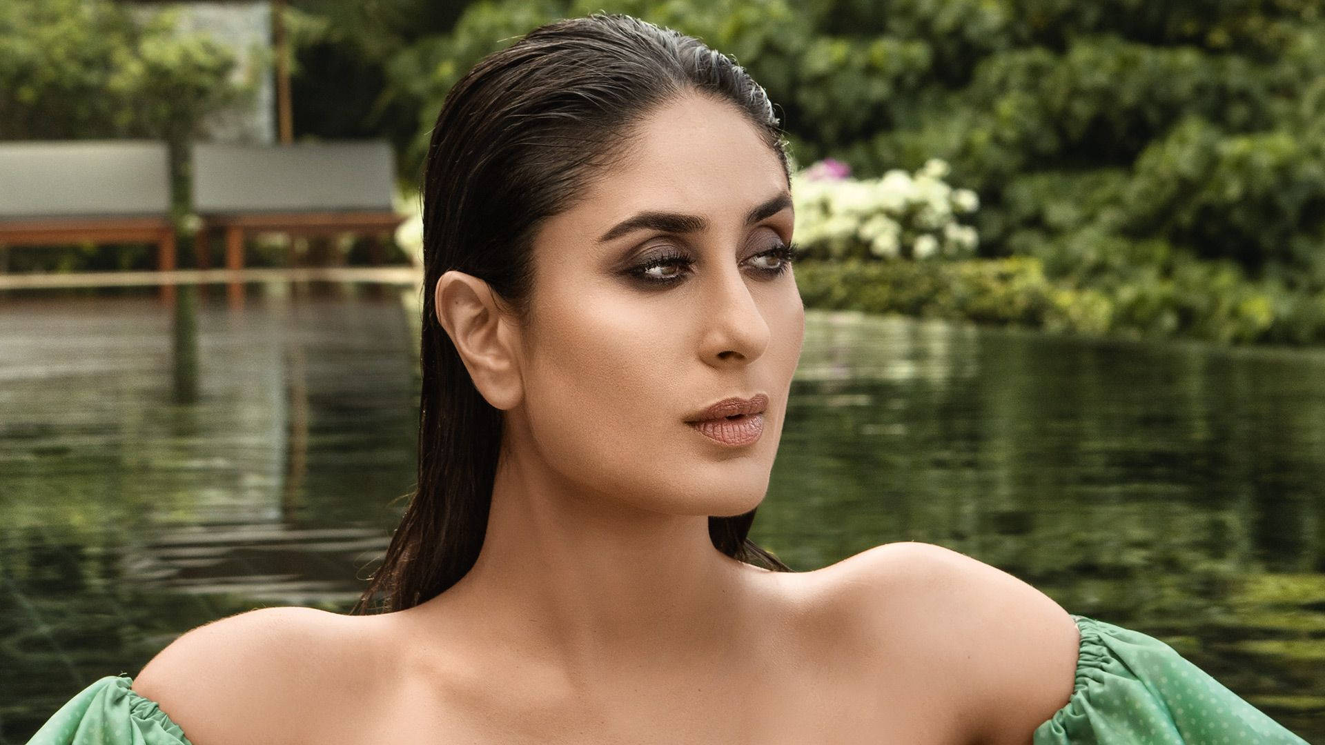 Kareena 桌布 壁紙 — 一位身穿綠色露肩連衣裙的女性在寧靜的泳池旁沉思，周圍環繞著茂密的綠植。