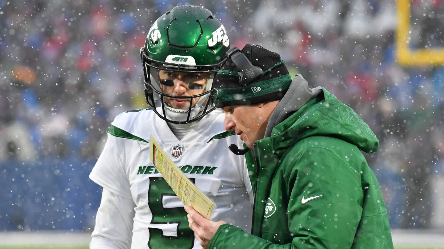 Ny Jets 桌布 壁紙 — 一位身穿綠色頭盔和白色球衣的紐約噴射機四分衛在比賽中下雪時與身穿綠色外套的教練商討。