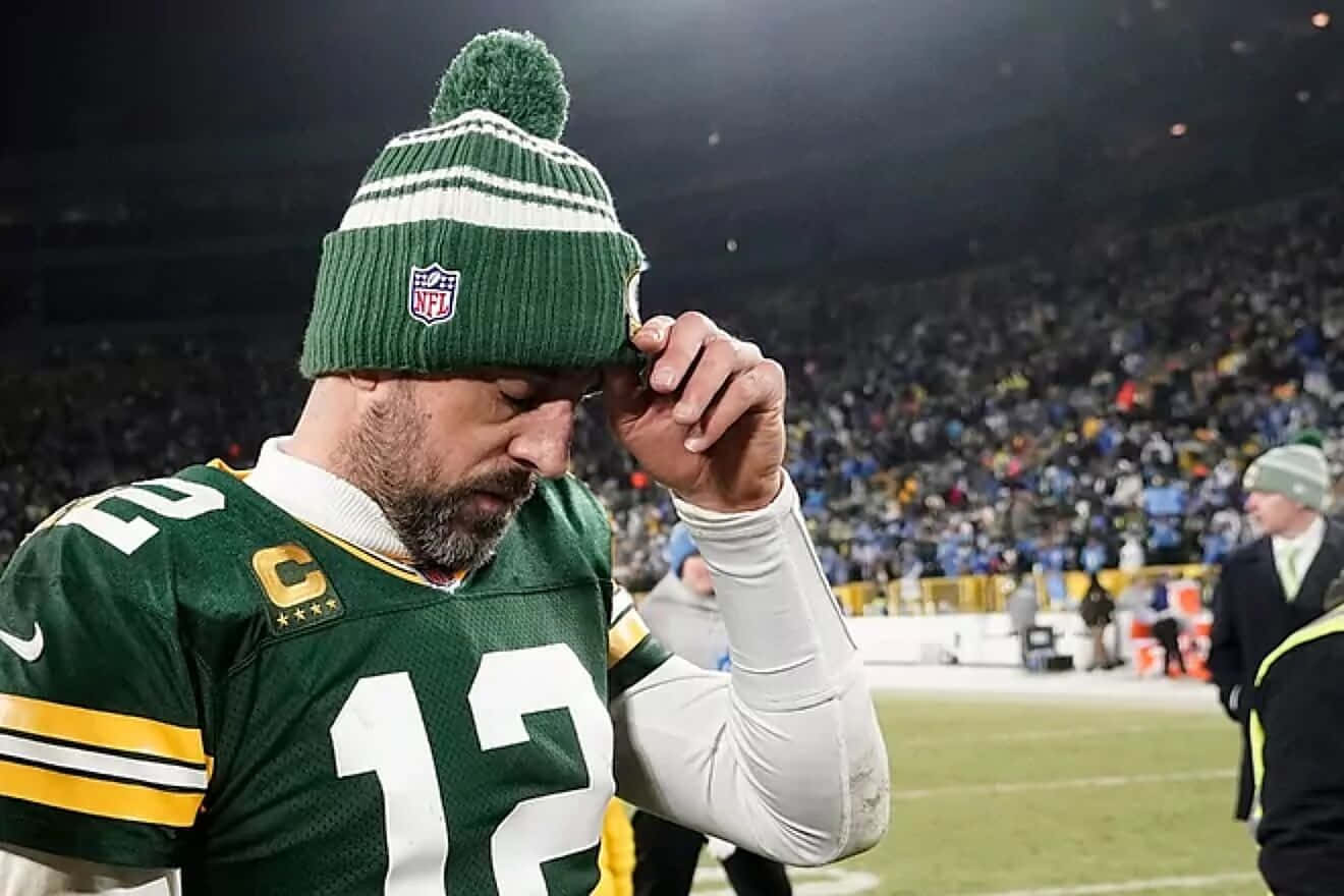 Aaron Rodgers 桌布 壁紙 — 一位身穿綠金球衣的綠灣包裝工四分衛在明亮的燈光下，於積雪的球場上調整他的無邊帽。