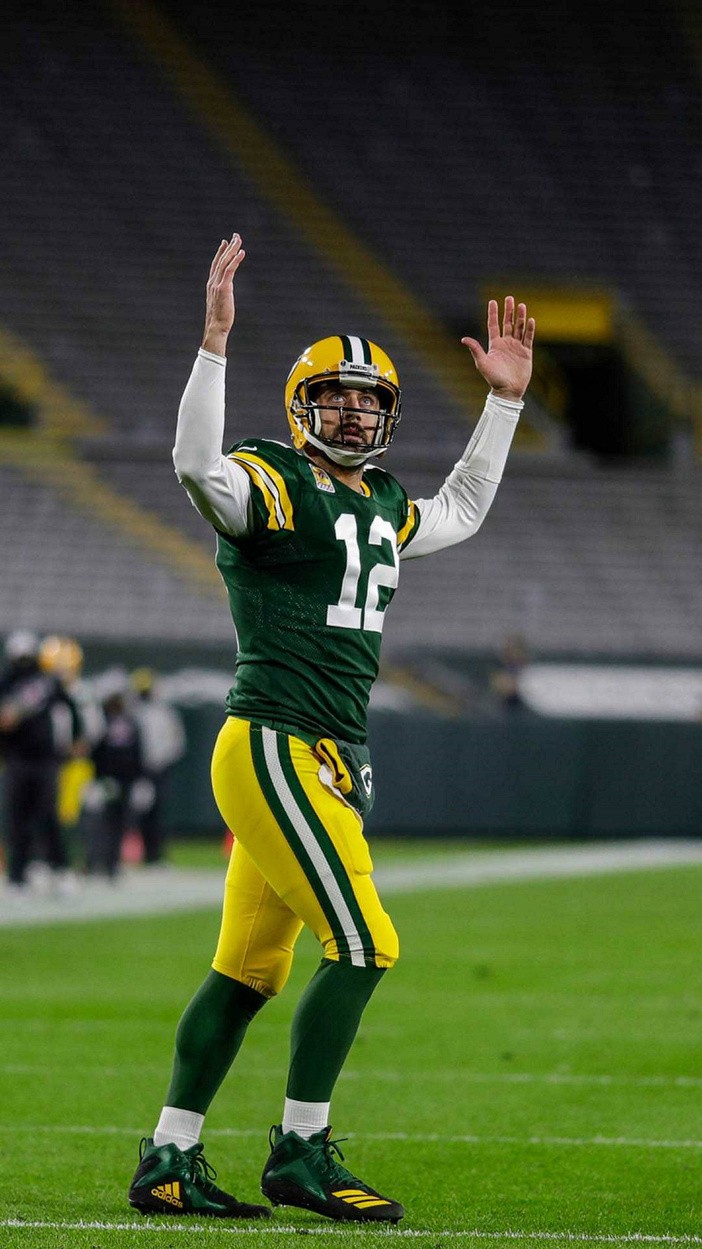 Aaron Rodgers 桌布 壁紙 — 一位身穿綠黃色球衣的綠灣包裝工四分衛在明亮燈光下的球場上向球迷揮手。