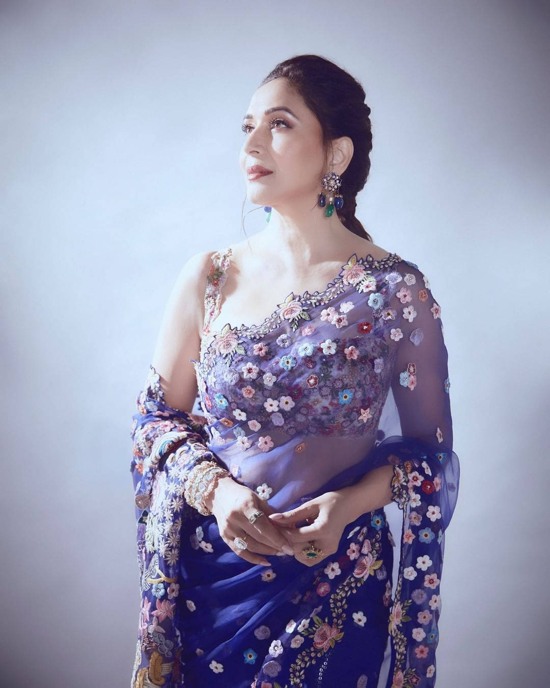 Madhuri Dixit 桌布 壁紙 — 一位身穿花卉刺繡藍色紗麗的女性在柔和的灰色攝影棚背景前優雅地擺姿勢。