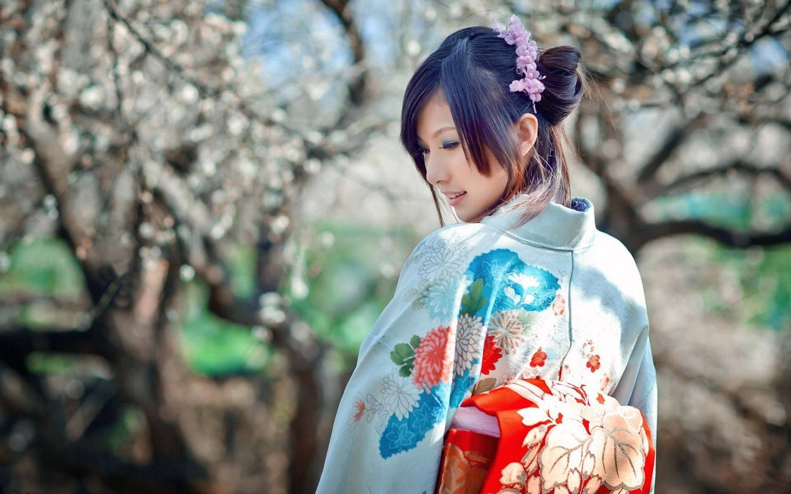 美女 桌布 壁紙 — 一位身穿花卉和服的女士站在盛開的櫻花樹下，柔和的光線穿過樹枝灑落。