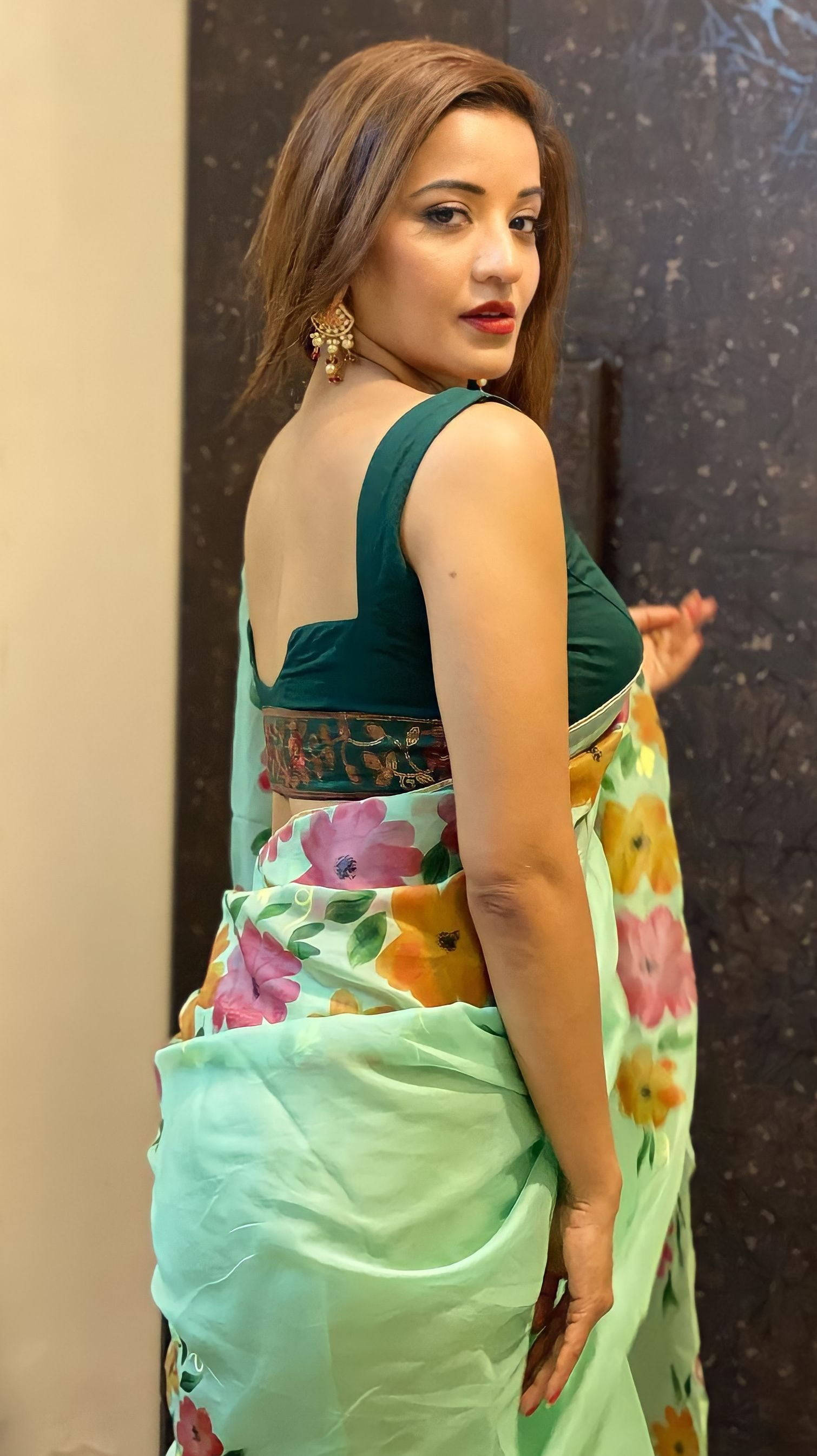 Bhojpuri 桌布 壁紙 — 一位身穿花卉圖案綠色紗麗和深綠色襯衫的女性，在紋理牆壁前優雅地擺姿勢。
